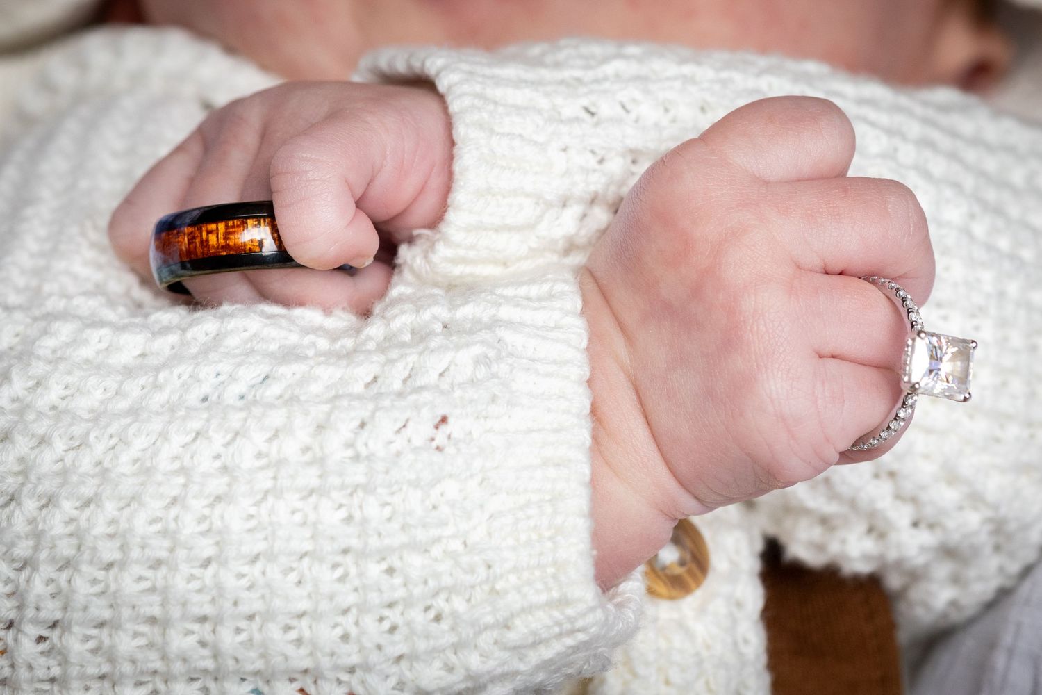 Close-up of tiny baby hands gripping a white knitted sweater with small buttons visible.