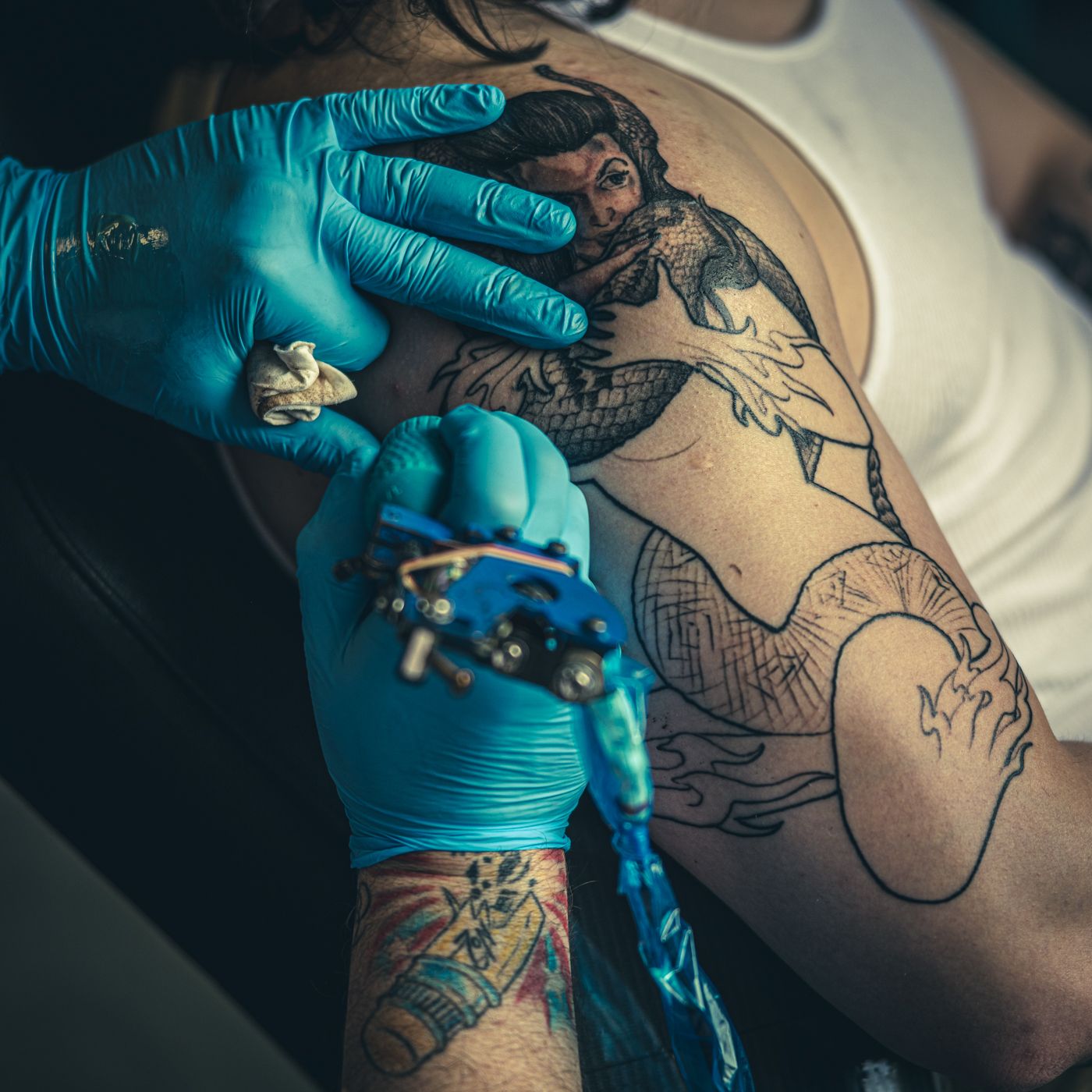 Close-up of tattoo artist working on detailed artwork with blue gloves.