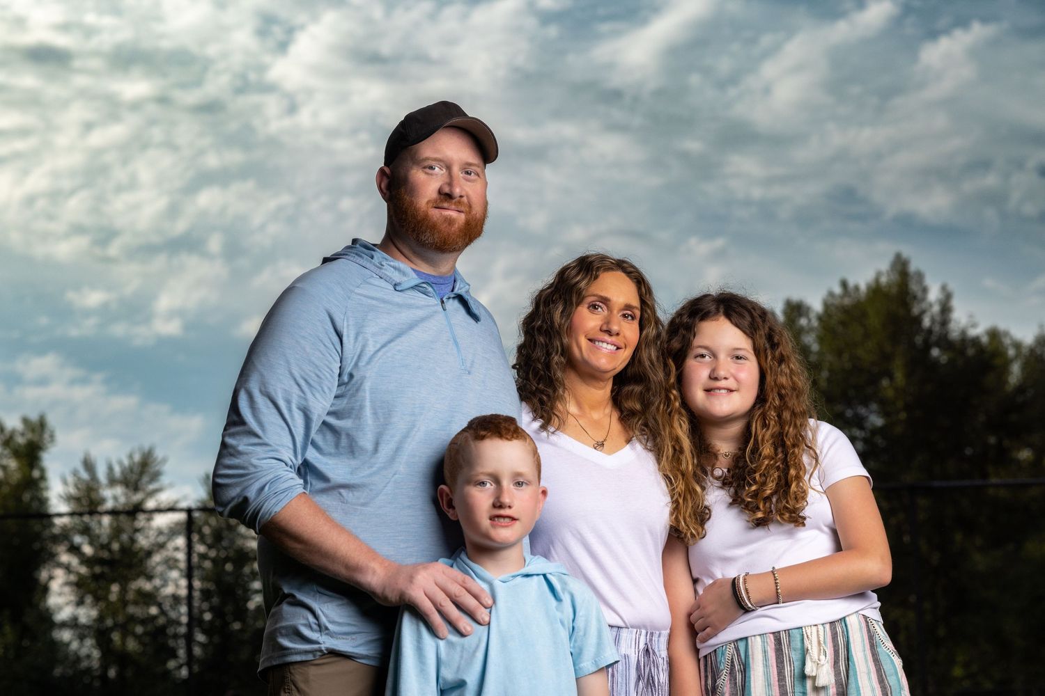 Family poses together outdoors on a cloudy day wearing coordinated blue and white outfits.