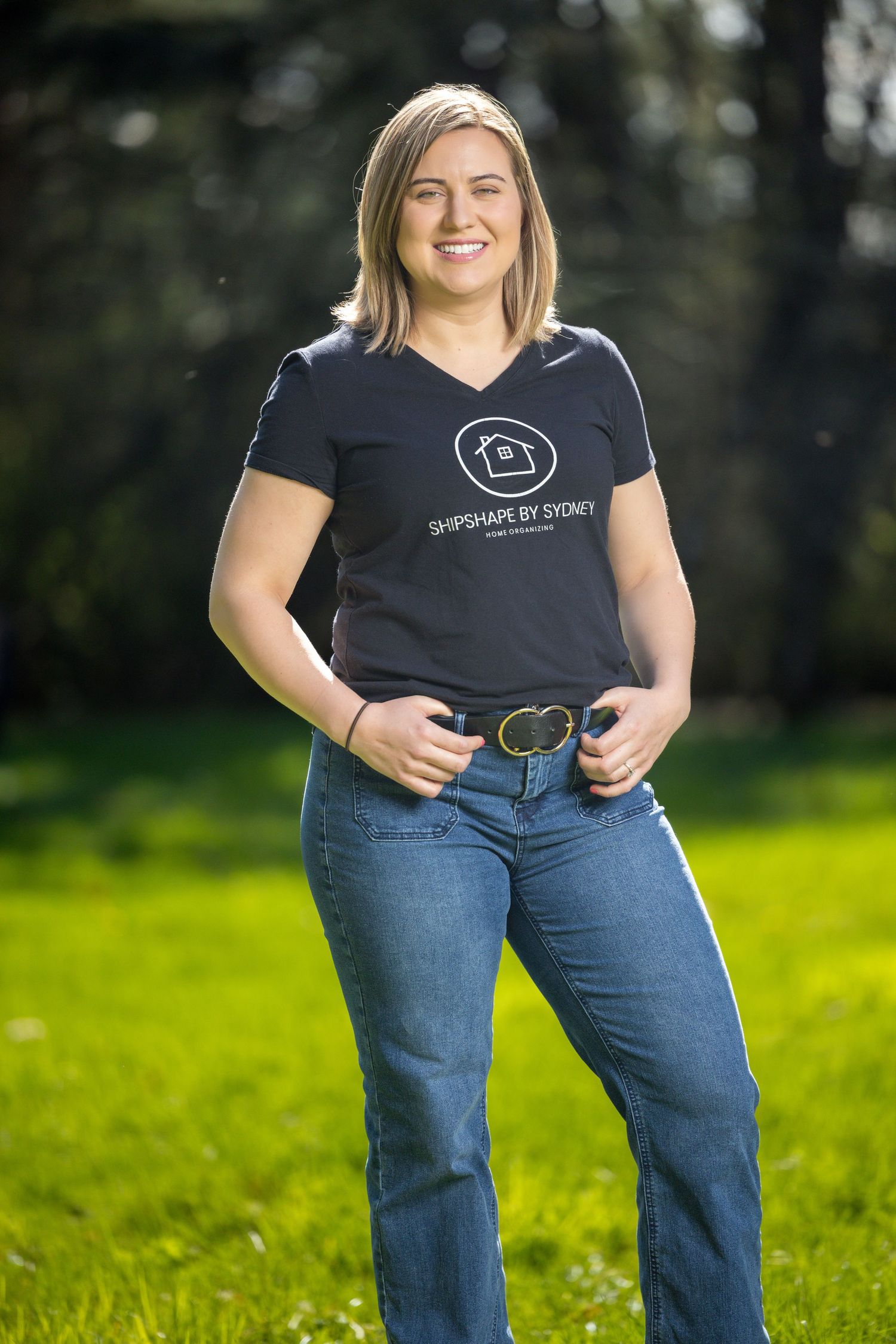 Person in black shirt and jeans standing on green grass outdoors.