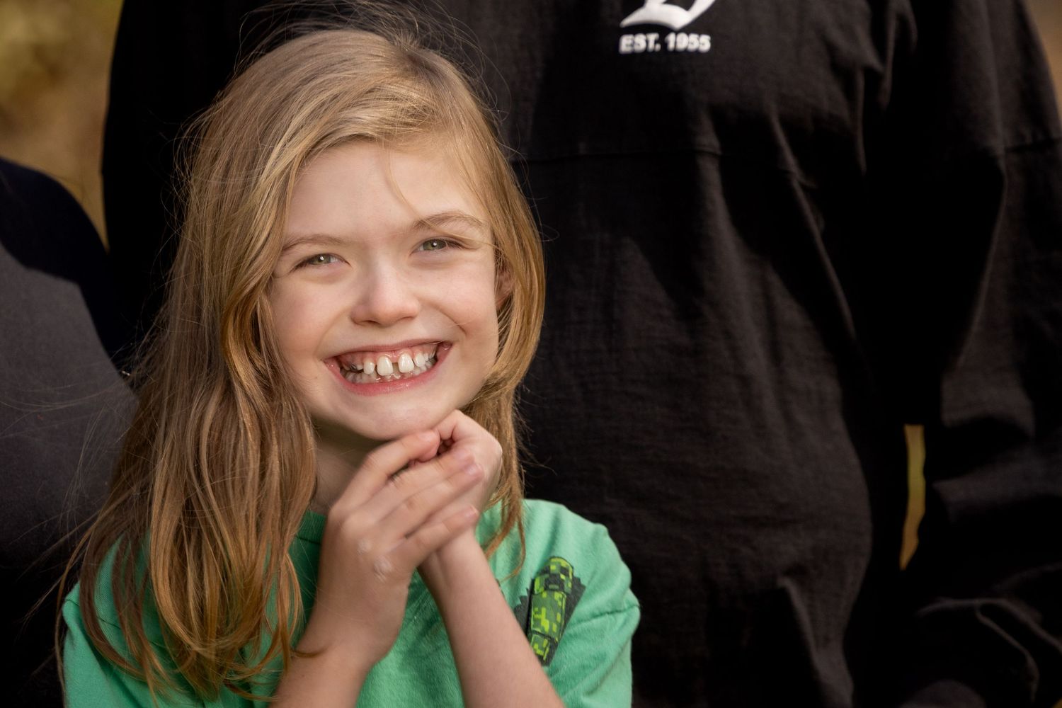 Young person in green shirt laughing joyfully against dark background.