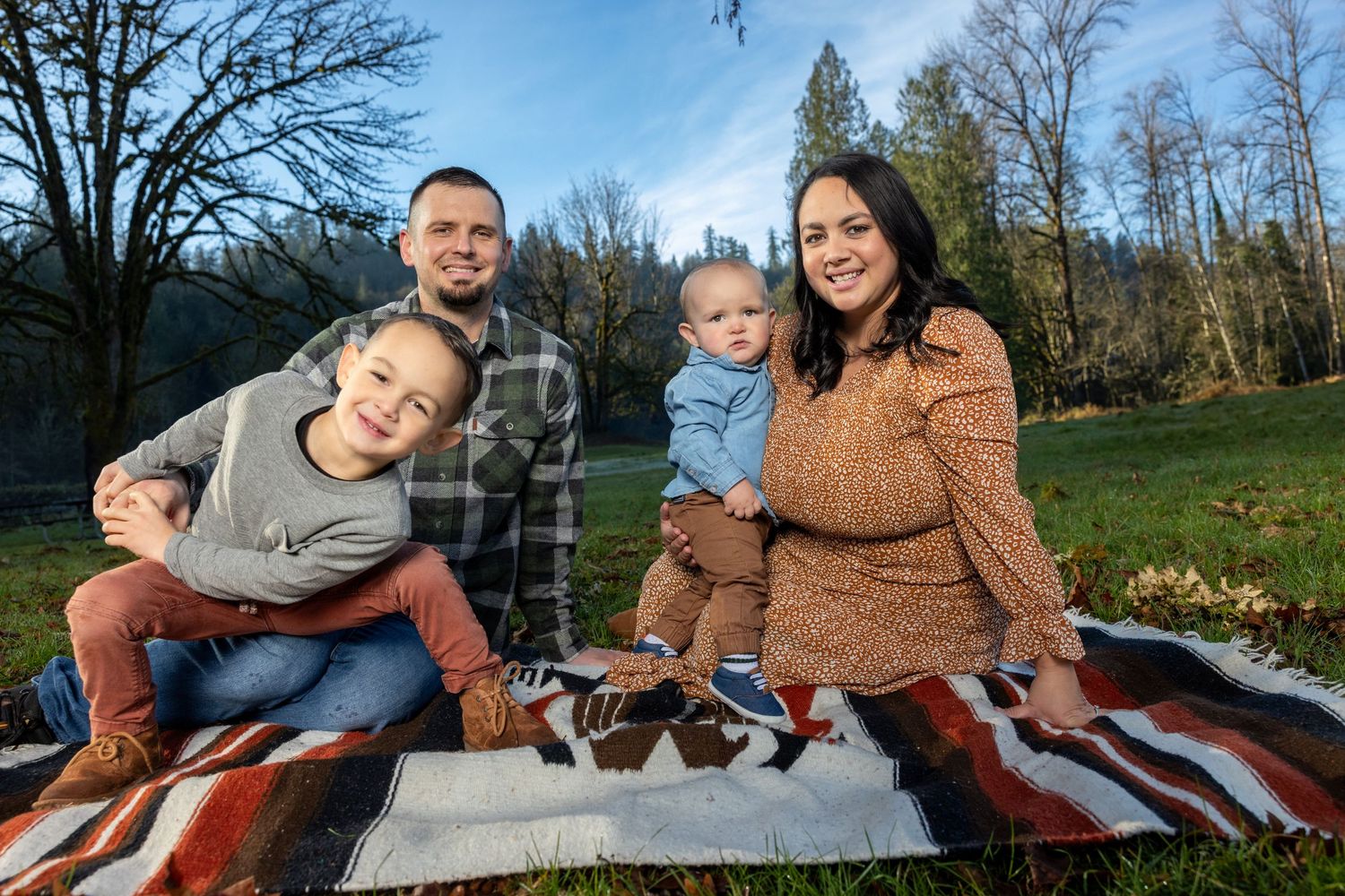 Family relaxing together on striped blanket during outdoor photo session.