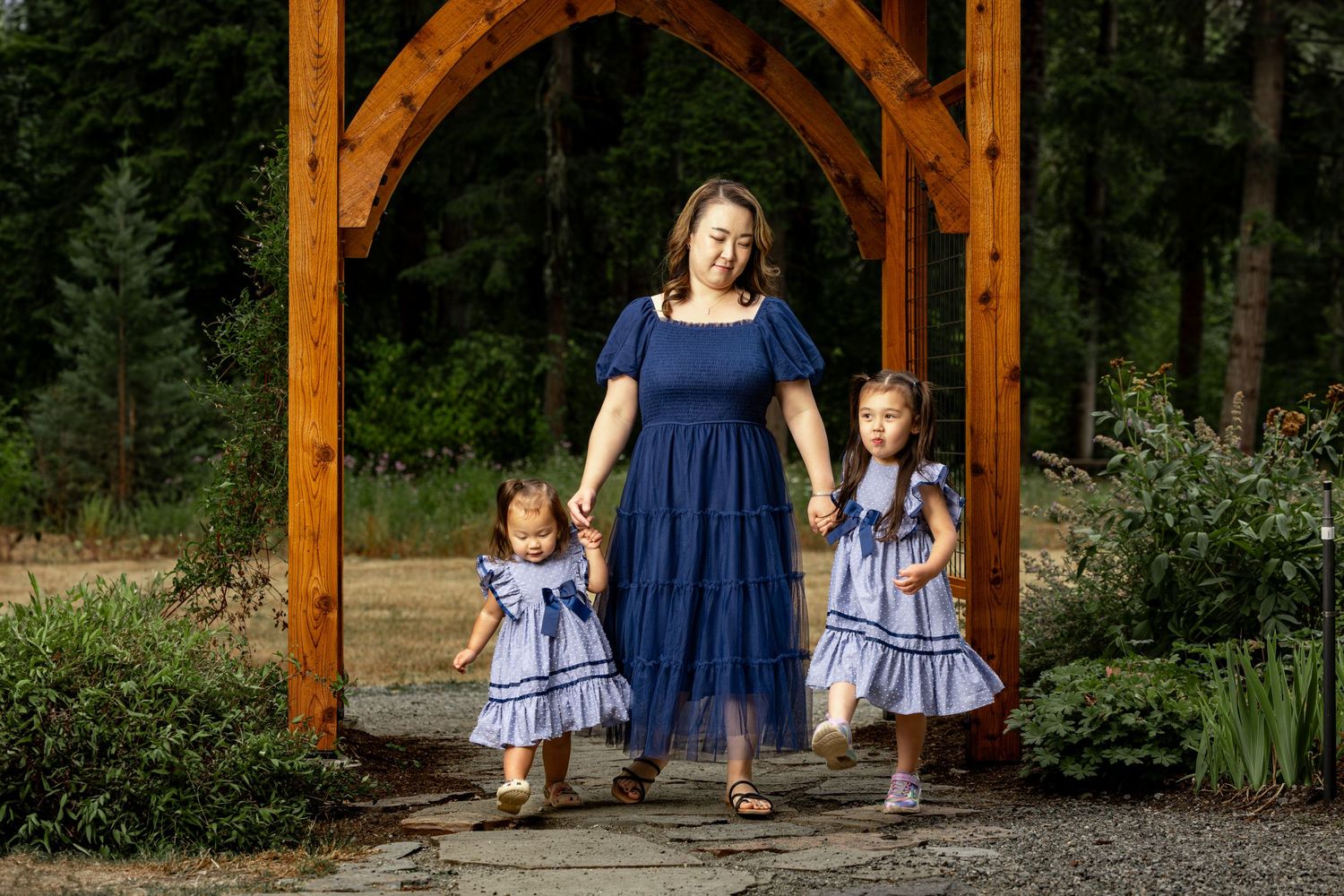 Young children in matching blue dresses playing in a garden with wooden beams overhead.