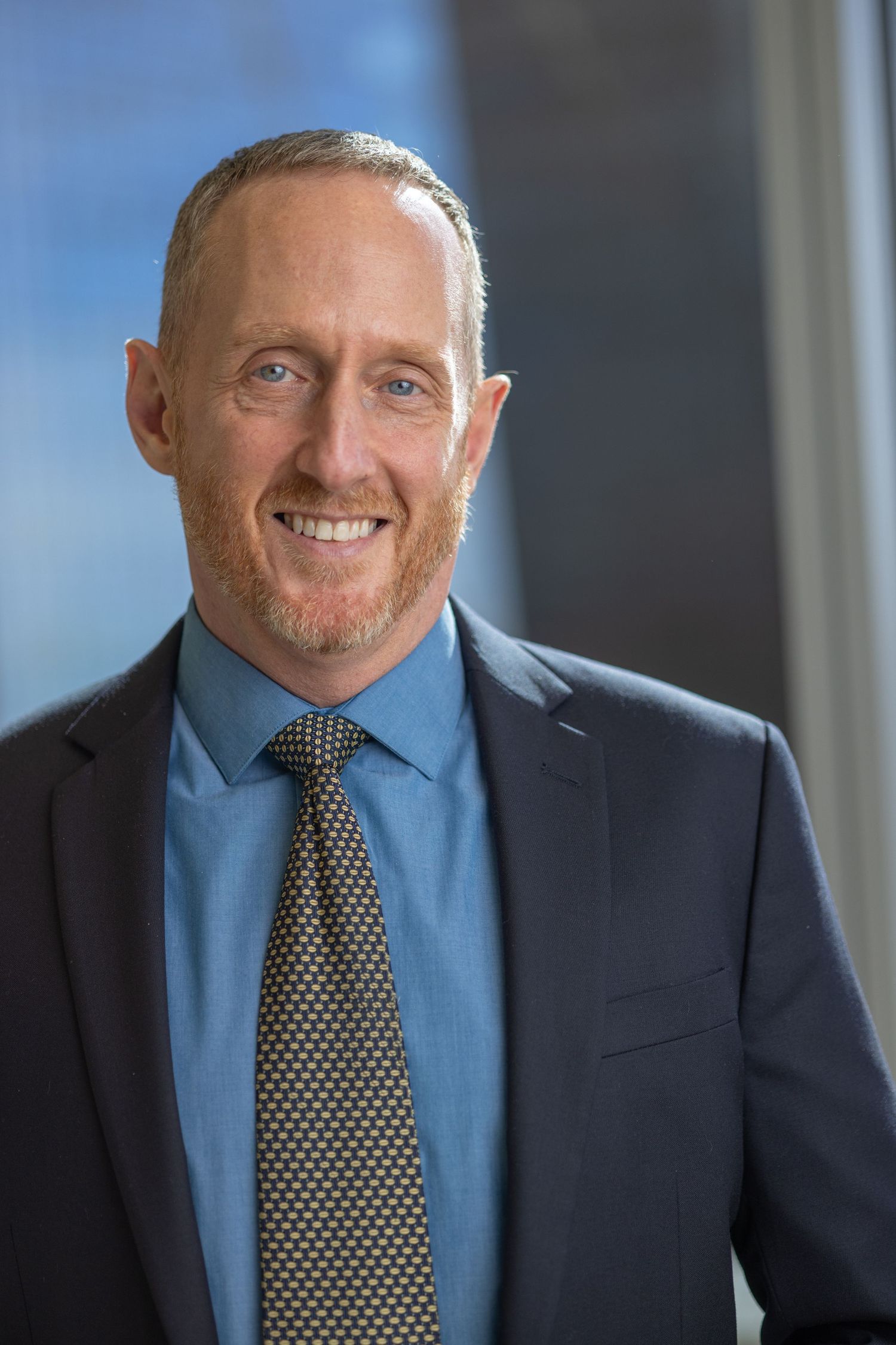 Business portraits of person in navy suit and polka dot tie with confident smile.