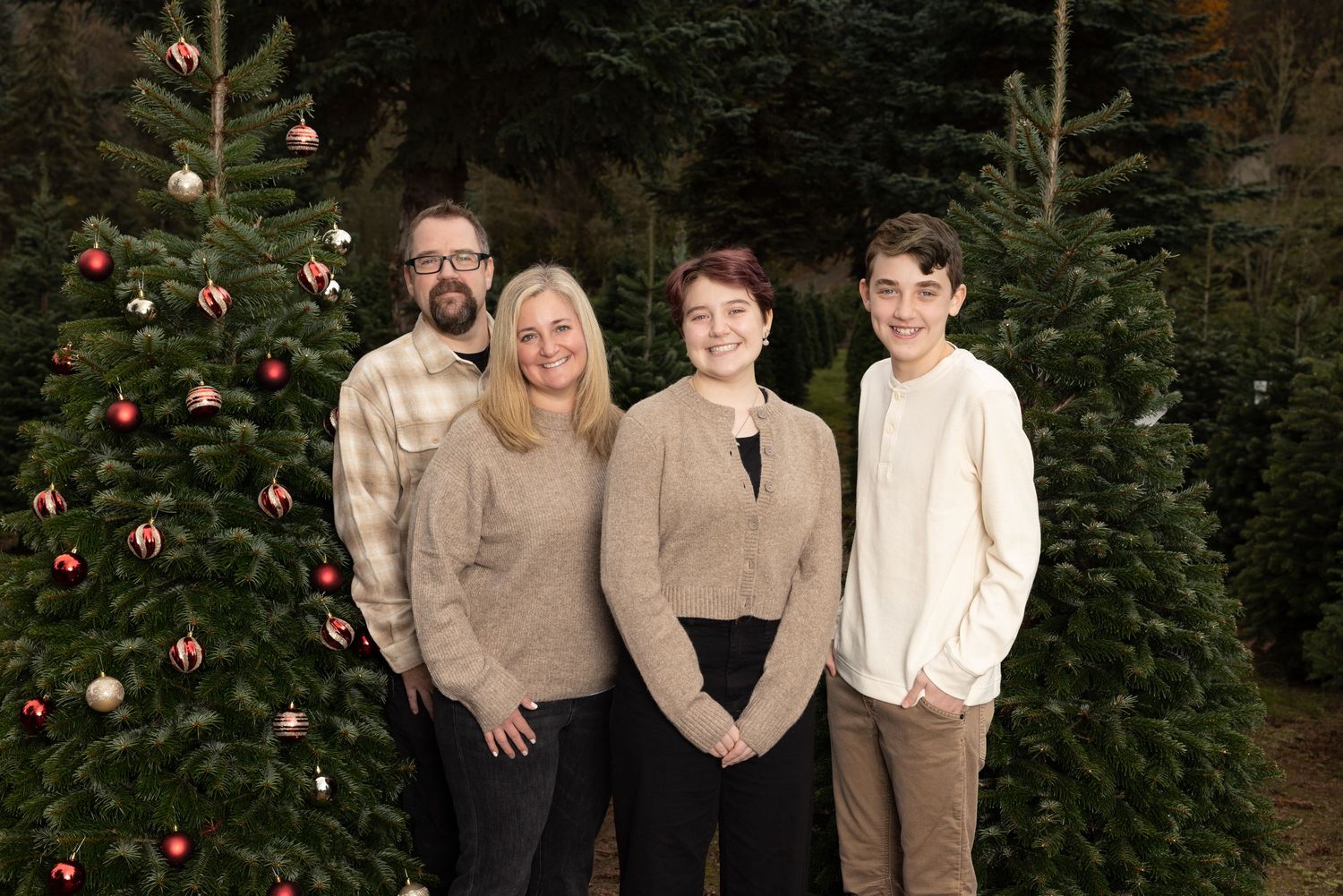 Family wearing coordinated neutral outfits poses by decorated Christmas tree.