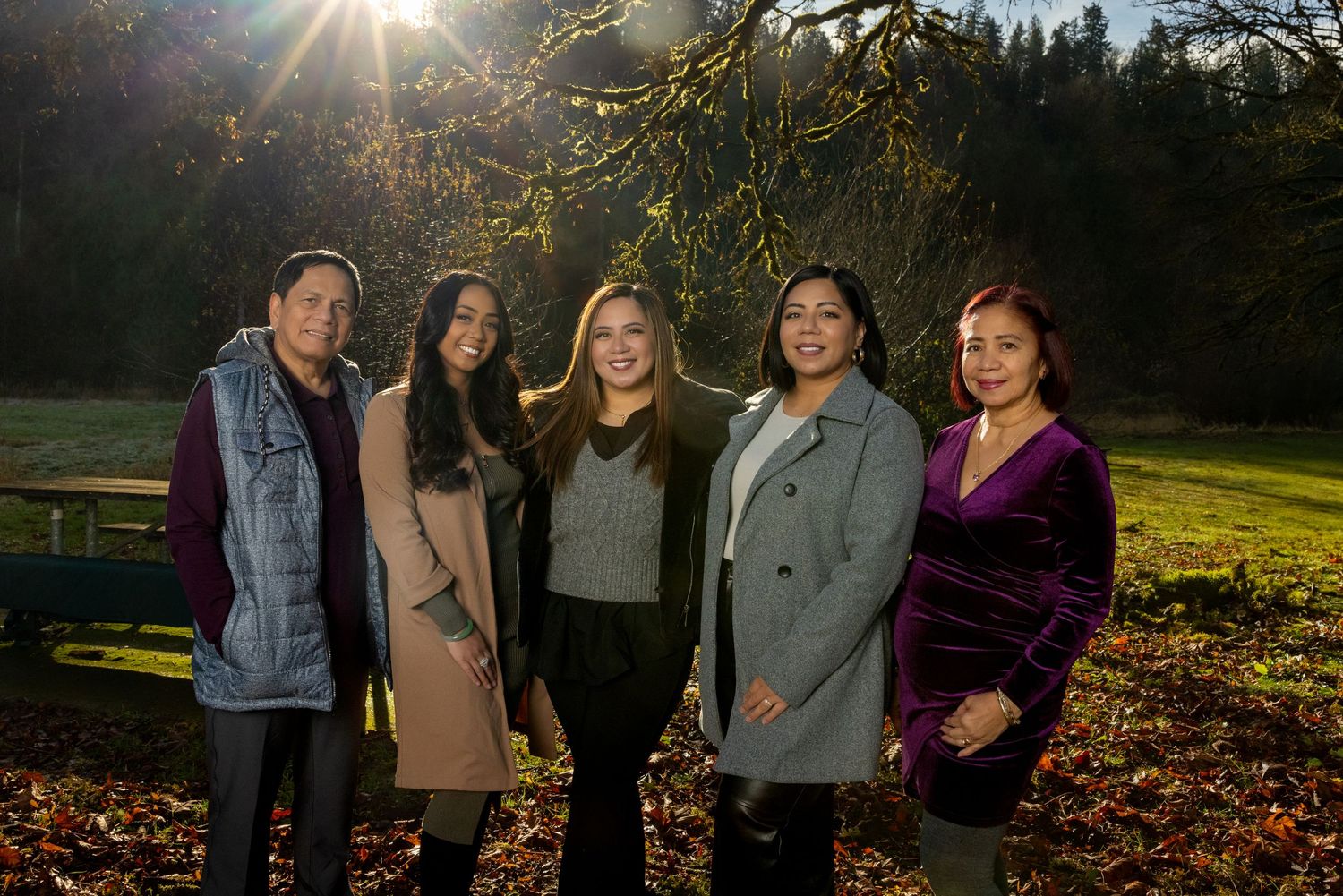 Outdoor family group photo with dramatic backlighting through trees at sunset.