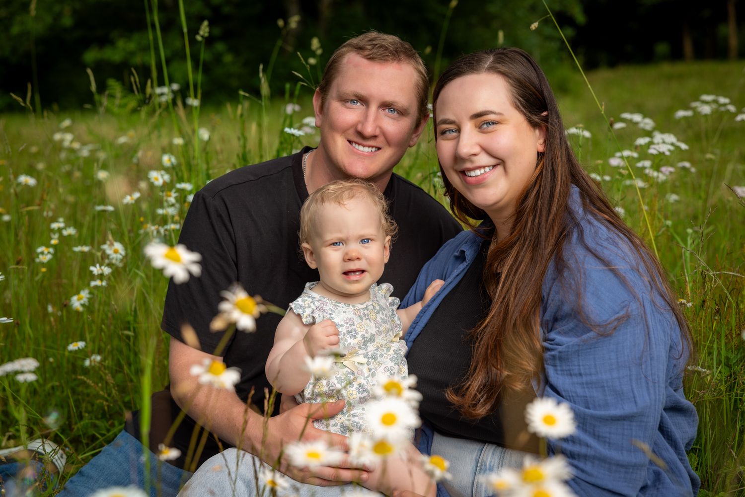 Family photo session in a meadow with blooming wildflowers on a sunny day.