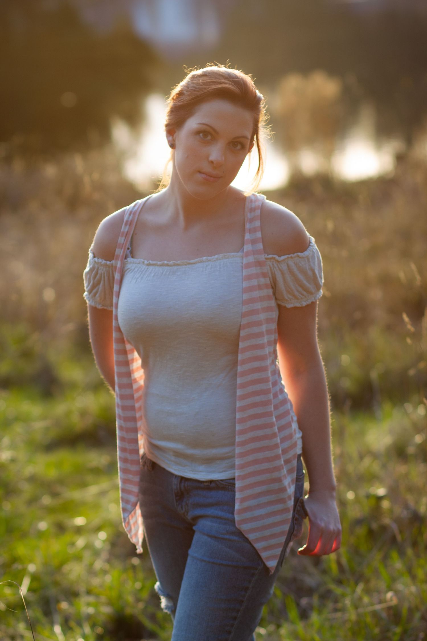 Casual outdoor portrait in golden sunlight showing jeans and striped cardigan outfit details.