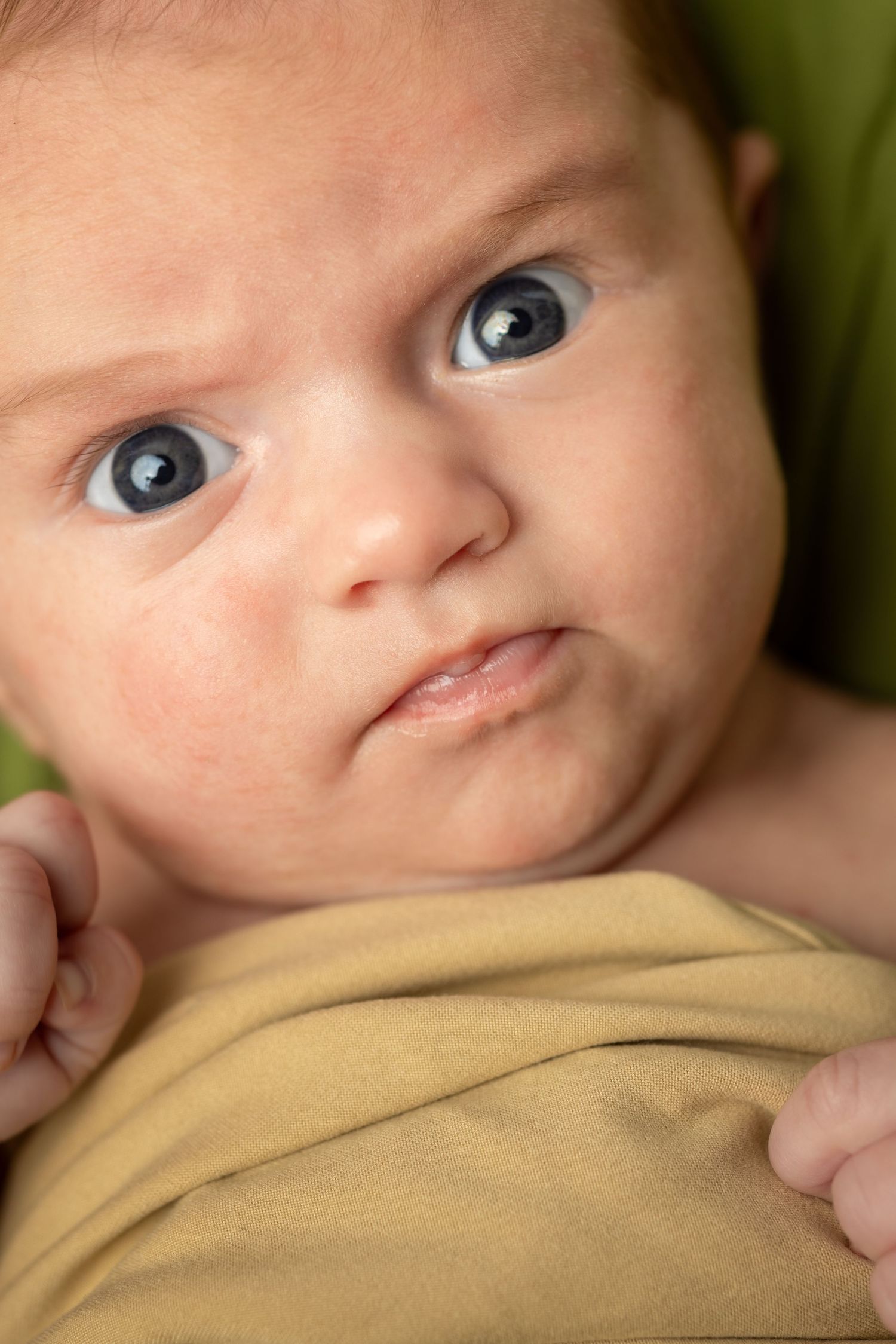 Close up portrait of infant with bright blue eyes wearing yellow clothing.