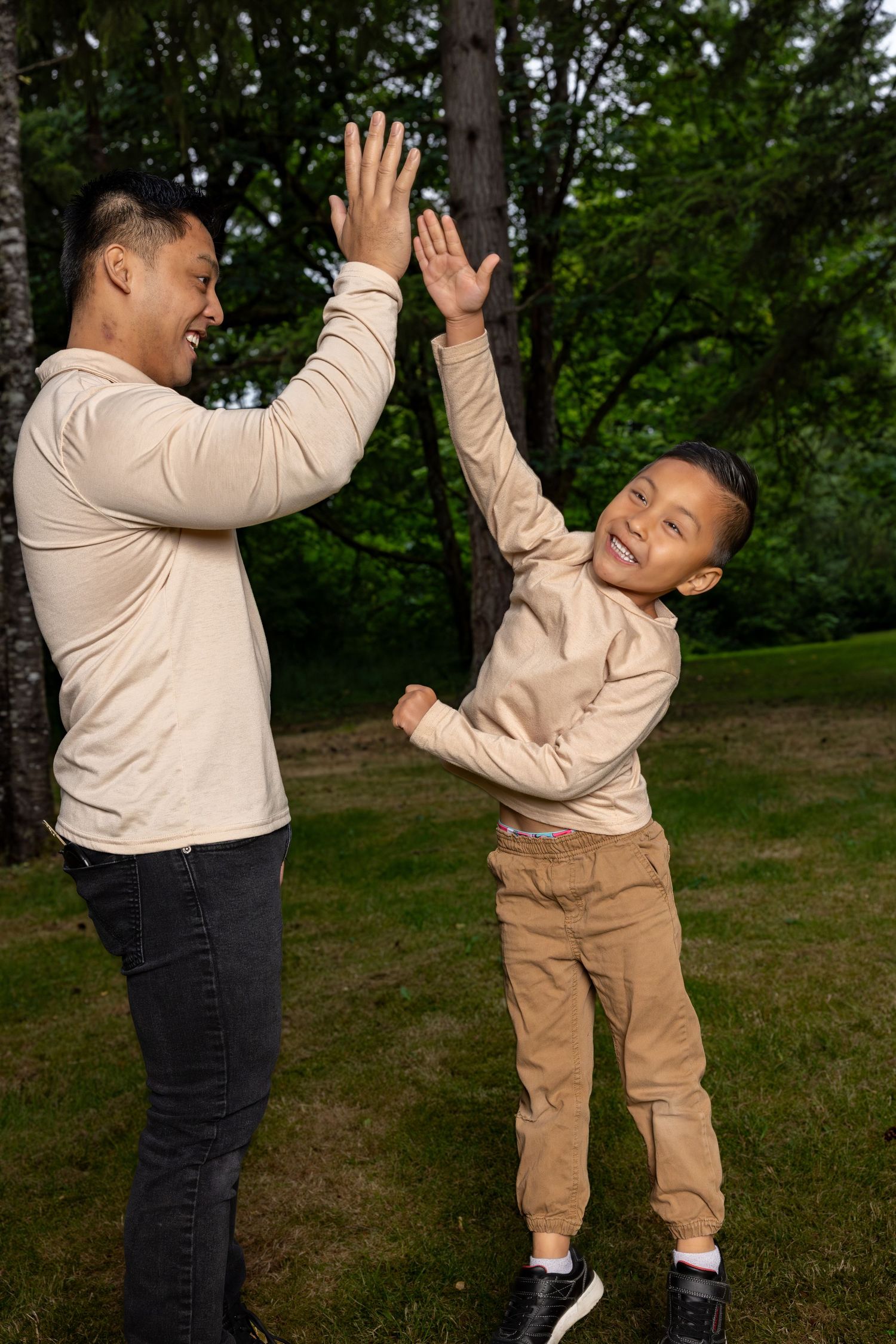 Playful sequence of parent and child high-fiving in casual attire against natural outdoor backdrop.