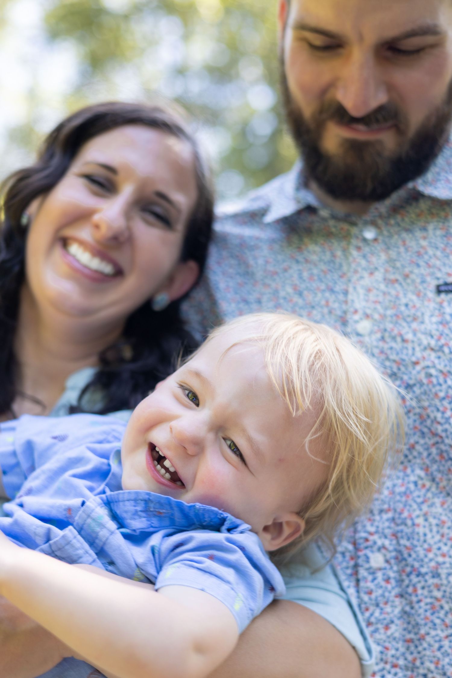 Joyful toddler laughs while being held by parents in outdoor setting.