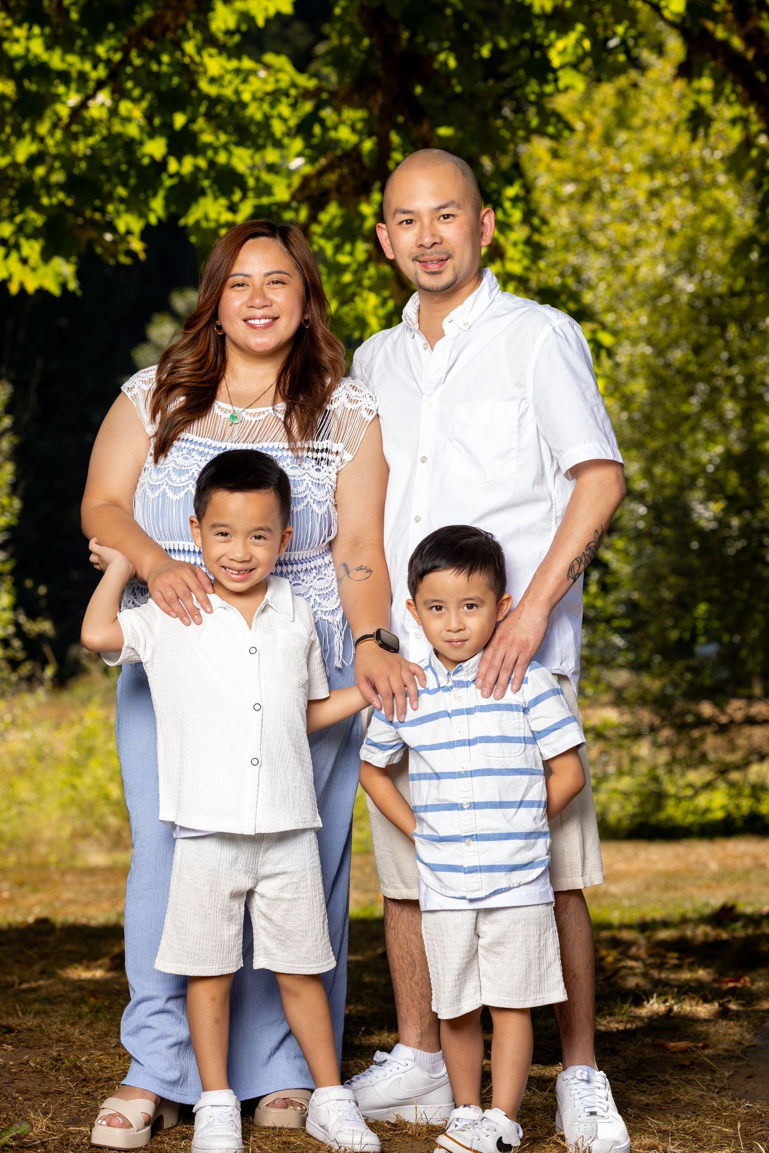 Family portrait session outdoors with casual attire against a natural backdrop of trees and sunlight.