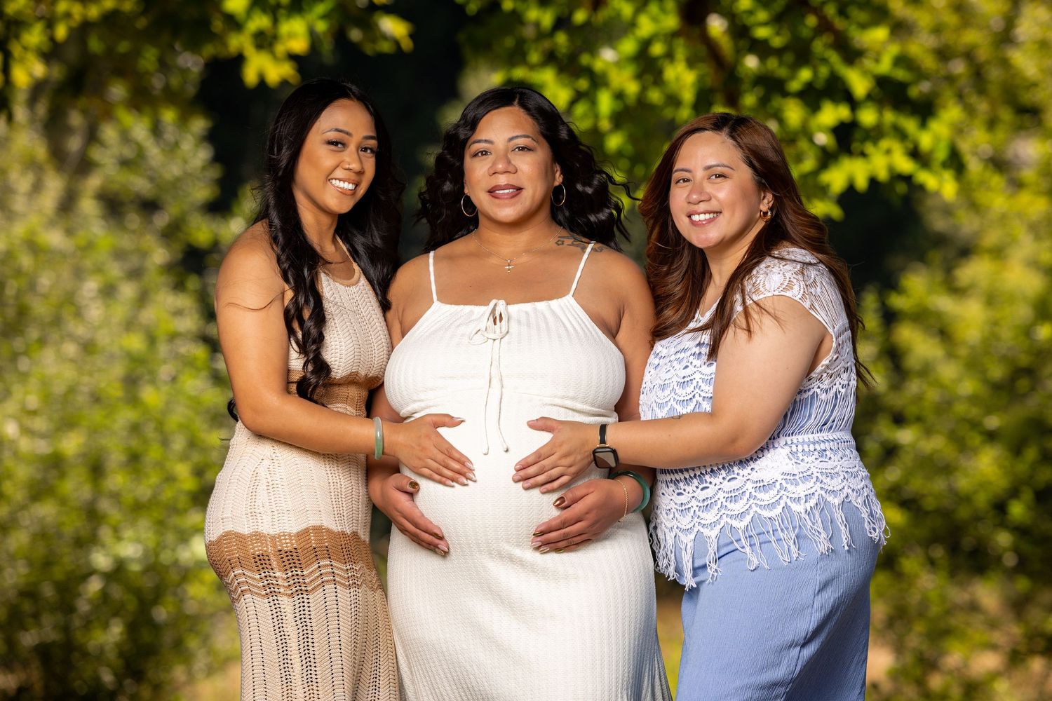 Three people in white and blue dresses posing together in a sunny outdoor setting.