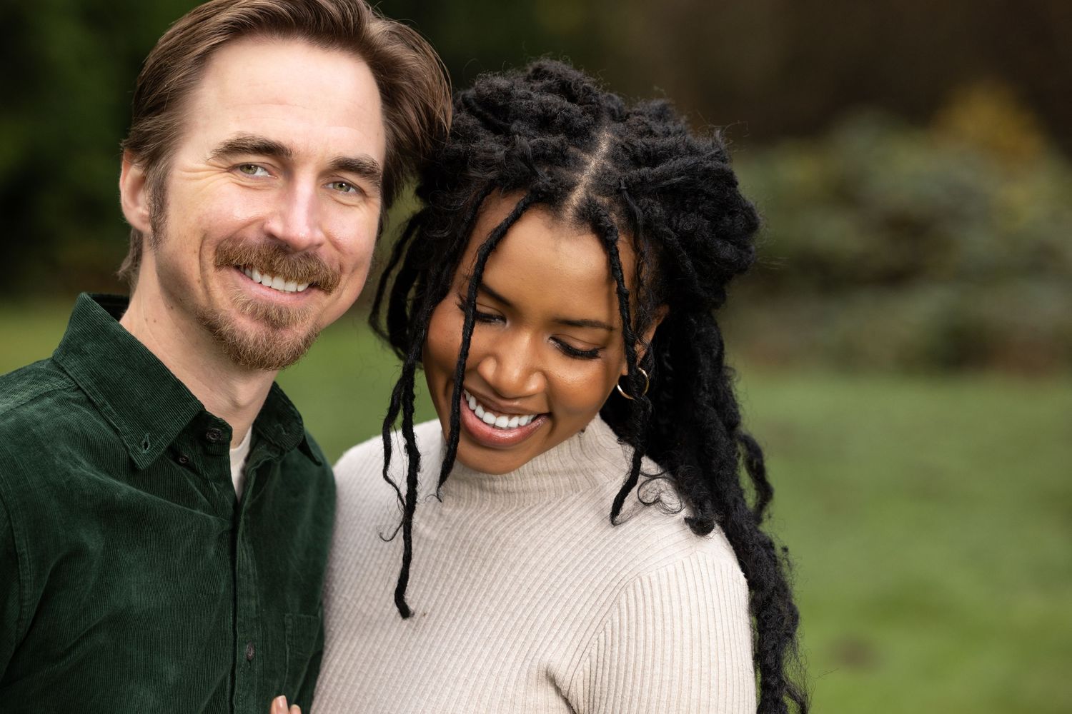 Couple shares intimate moments outdoors wearing cream and dark green clothing.
