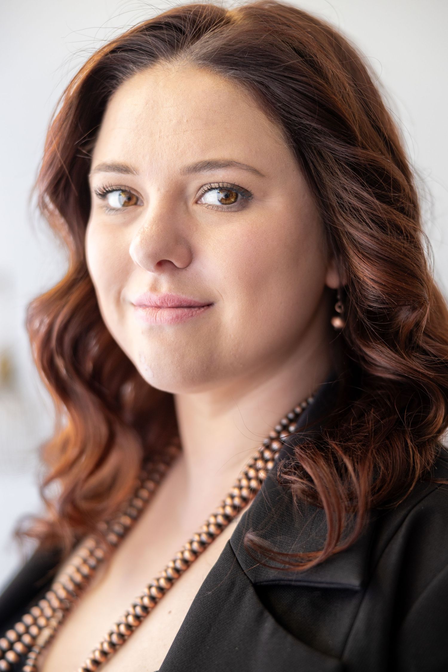 Professional portrait series with black blazer and beaded necklace against white background.