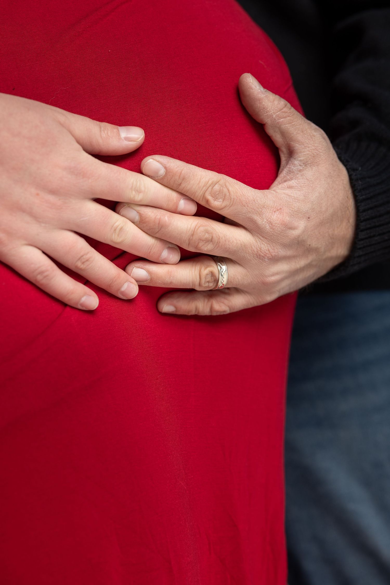 Close-up of hands resting on pregnant belly in red maternity dress.