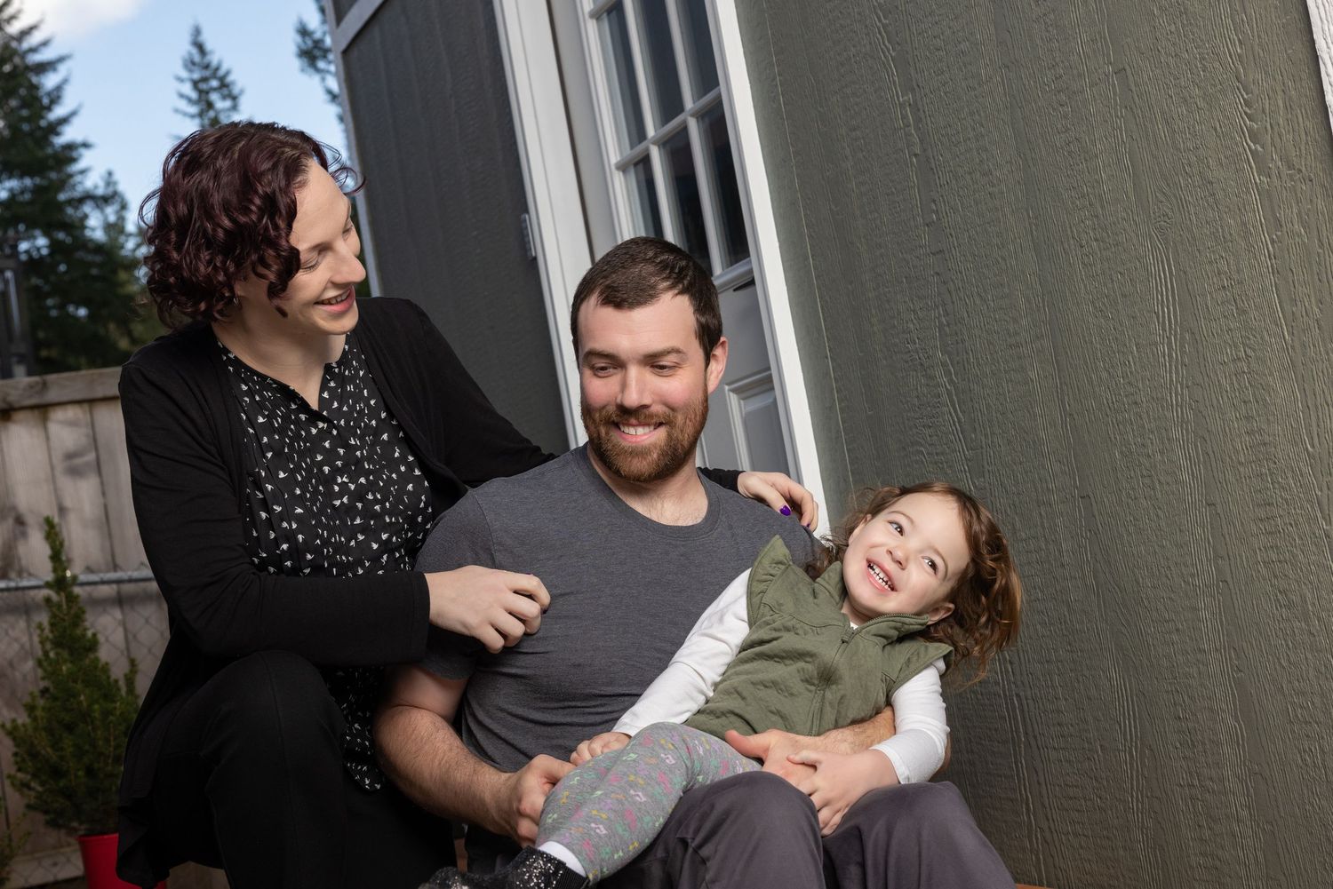 Family shares candid moments during an outdoor photo session against a grey wall.