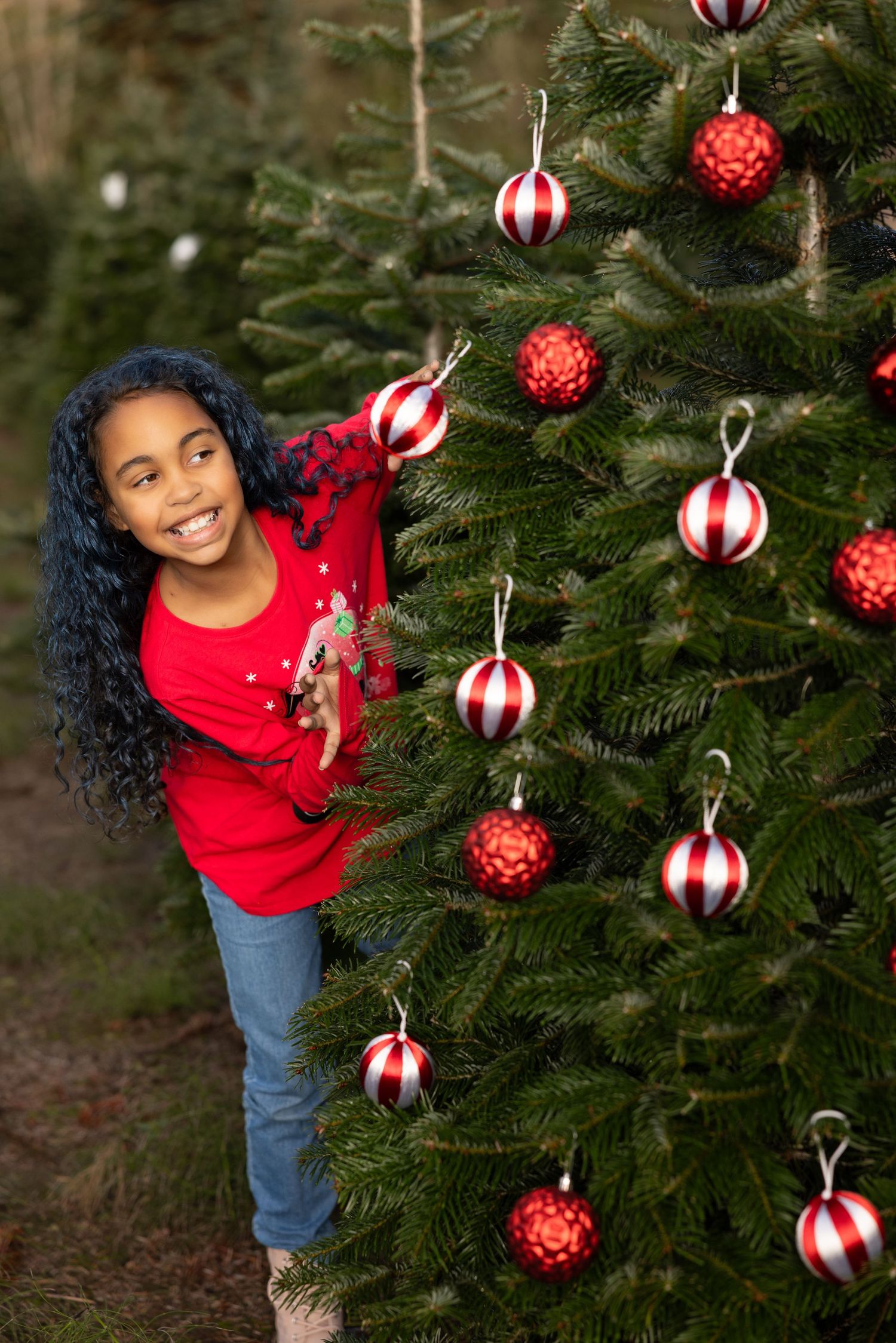 Child decorating Christmas tree with red and white striped ornaments.