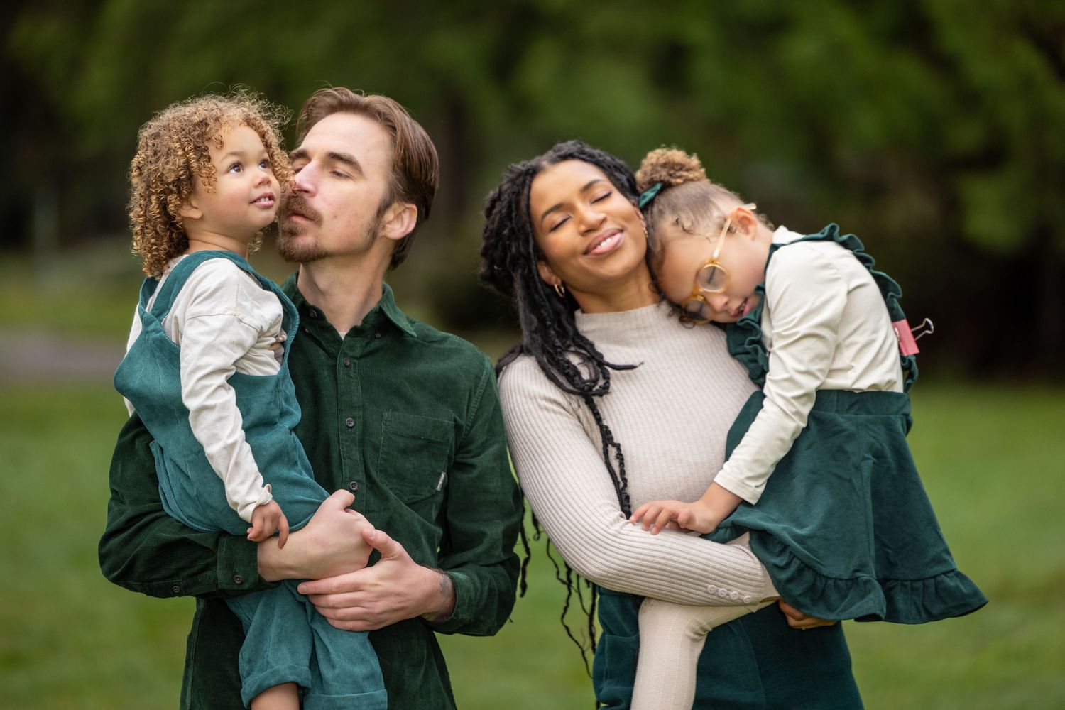 Family shares joyful embraces during outdoor photo session in a park.