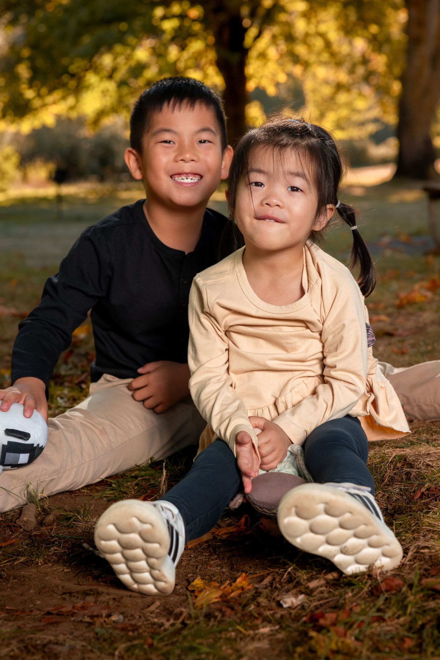Two children sitting together on autumn ground covered in fallen leaves.