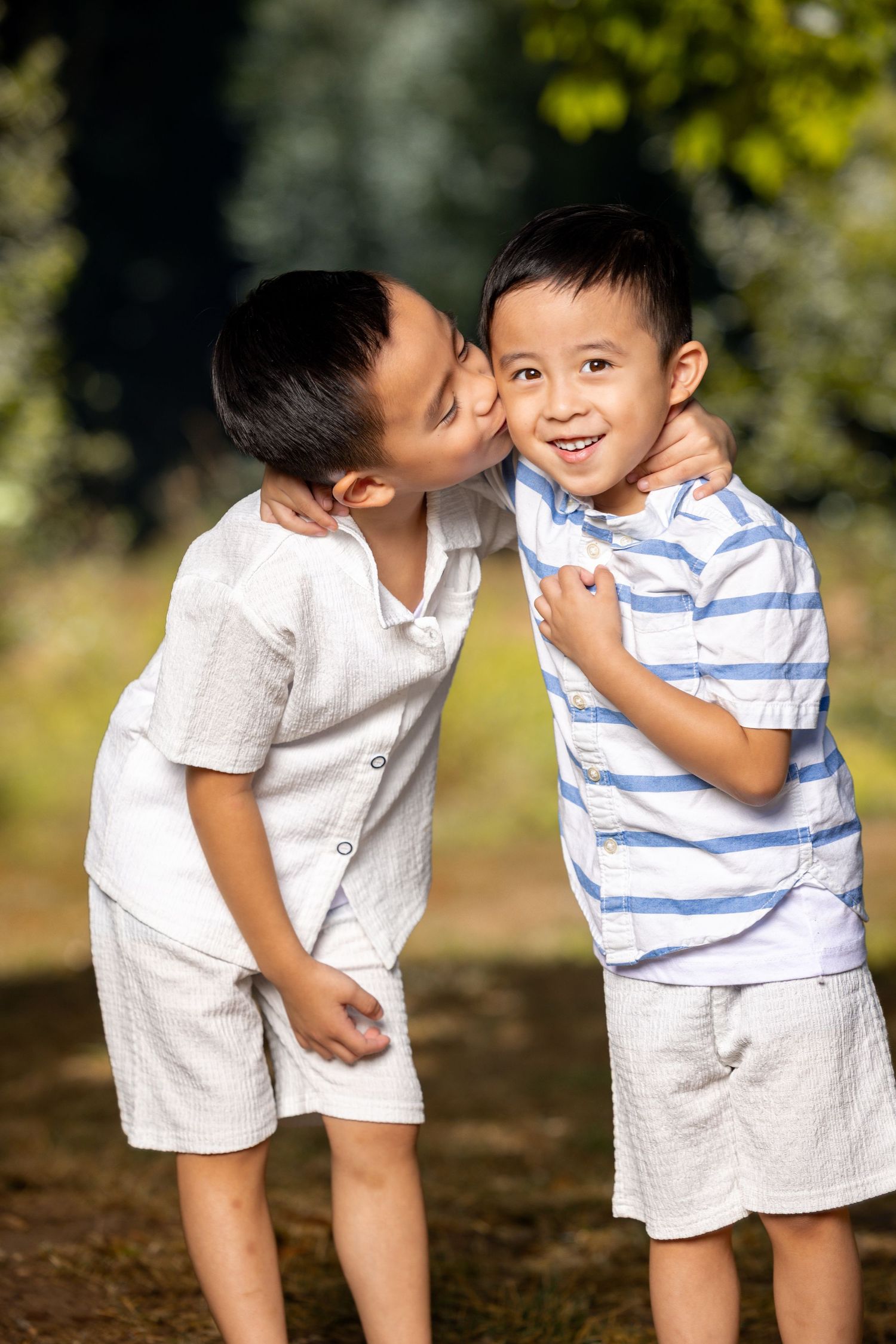 Two children in white and striped summer outfits share a playful moment outdoors.