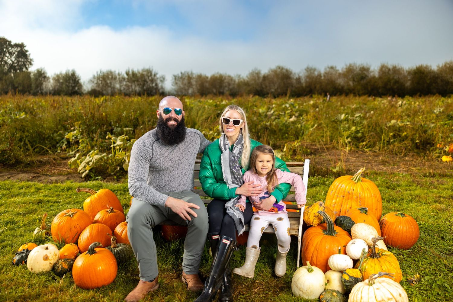 Family sitting among pumpkins and gourds at autumn harvest patch.