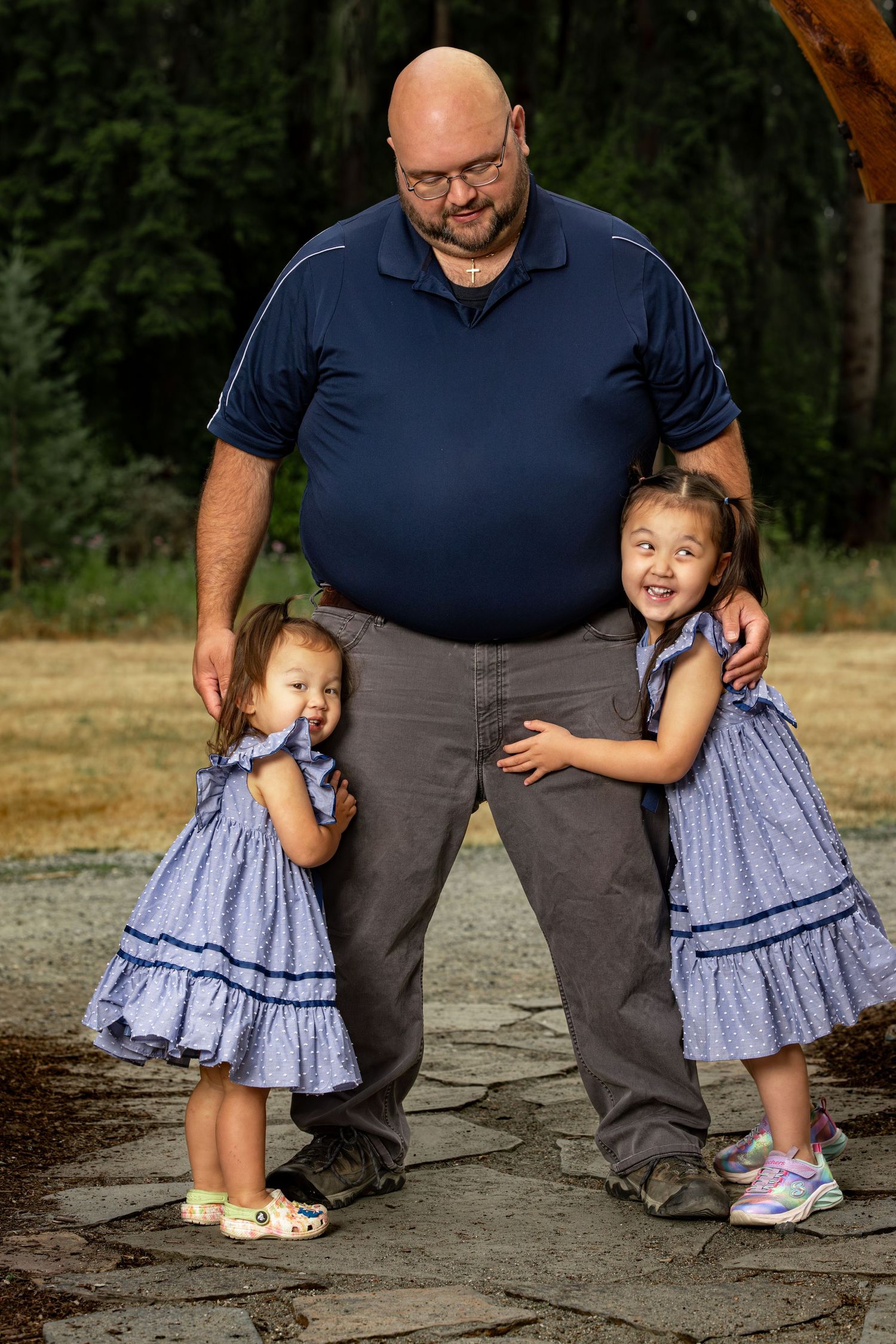 Two young girls in matching blue dresses pose with adult in casual outdoor setting.