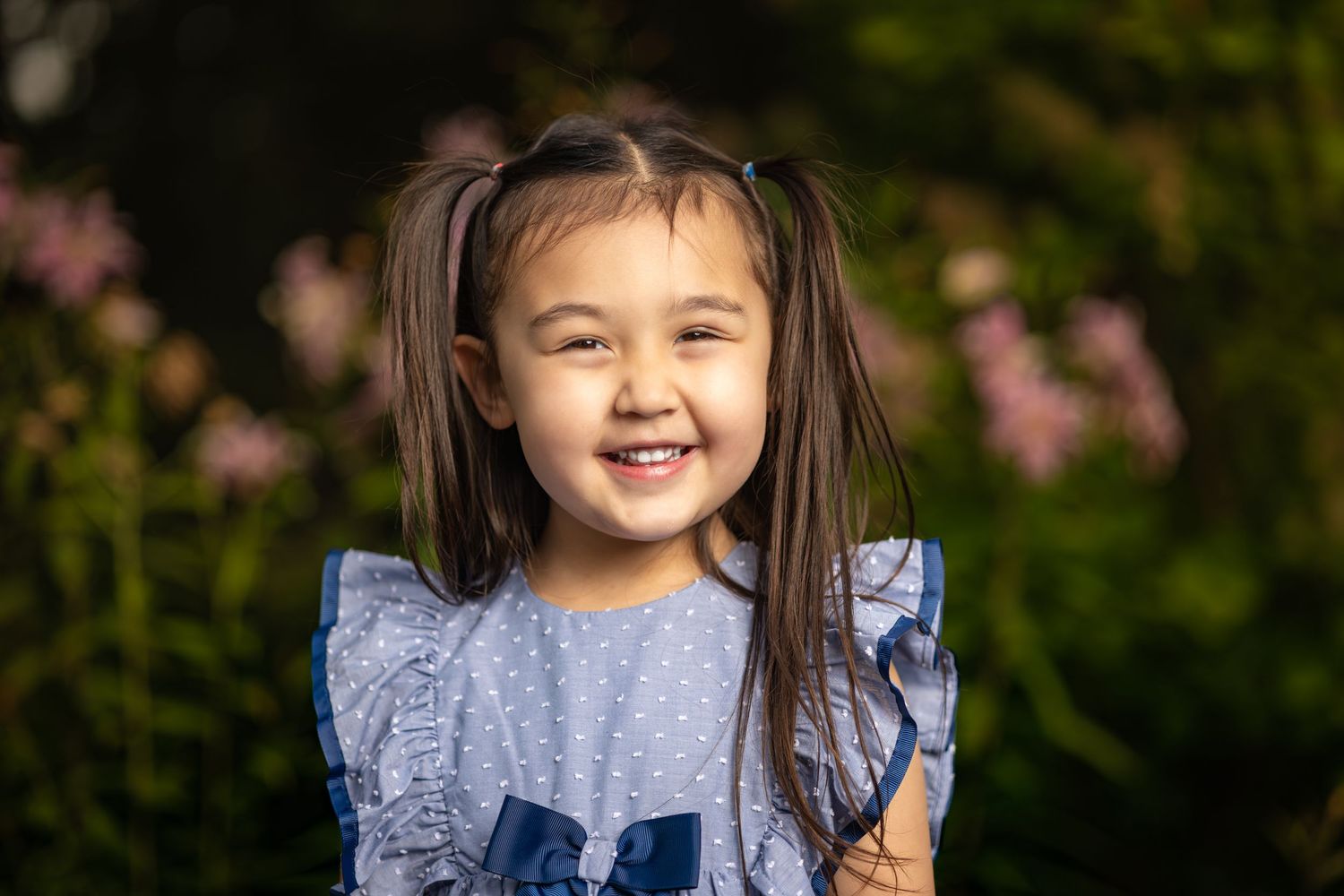 Child in blue ruffled dress photographed outdoors with cherry blossoms in background.
