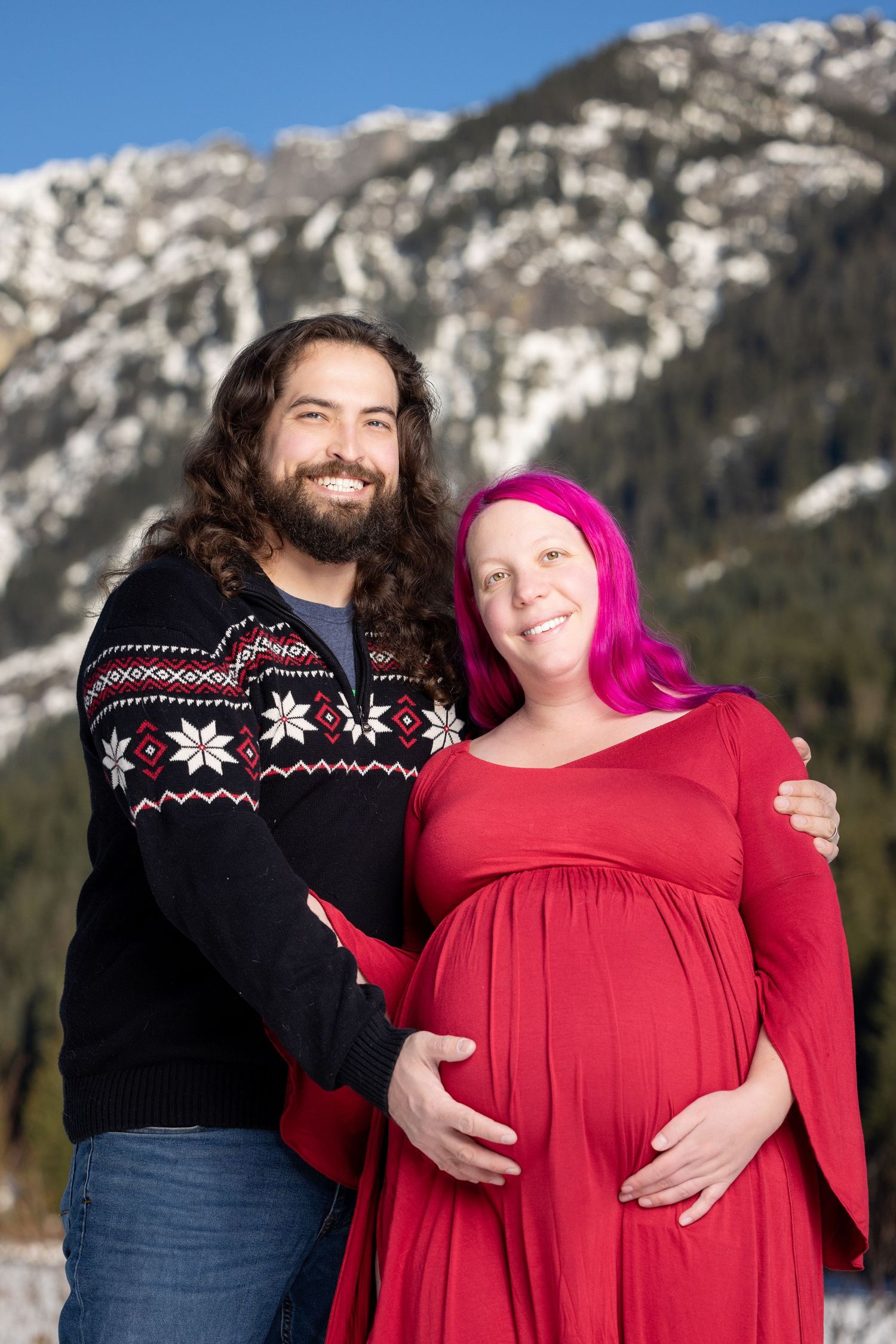Couple's winter maternity photoshoot featuring a red dress and Nordic sweater.
