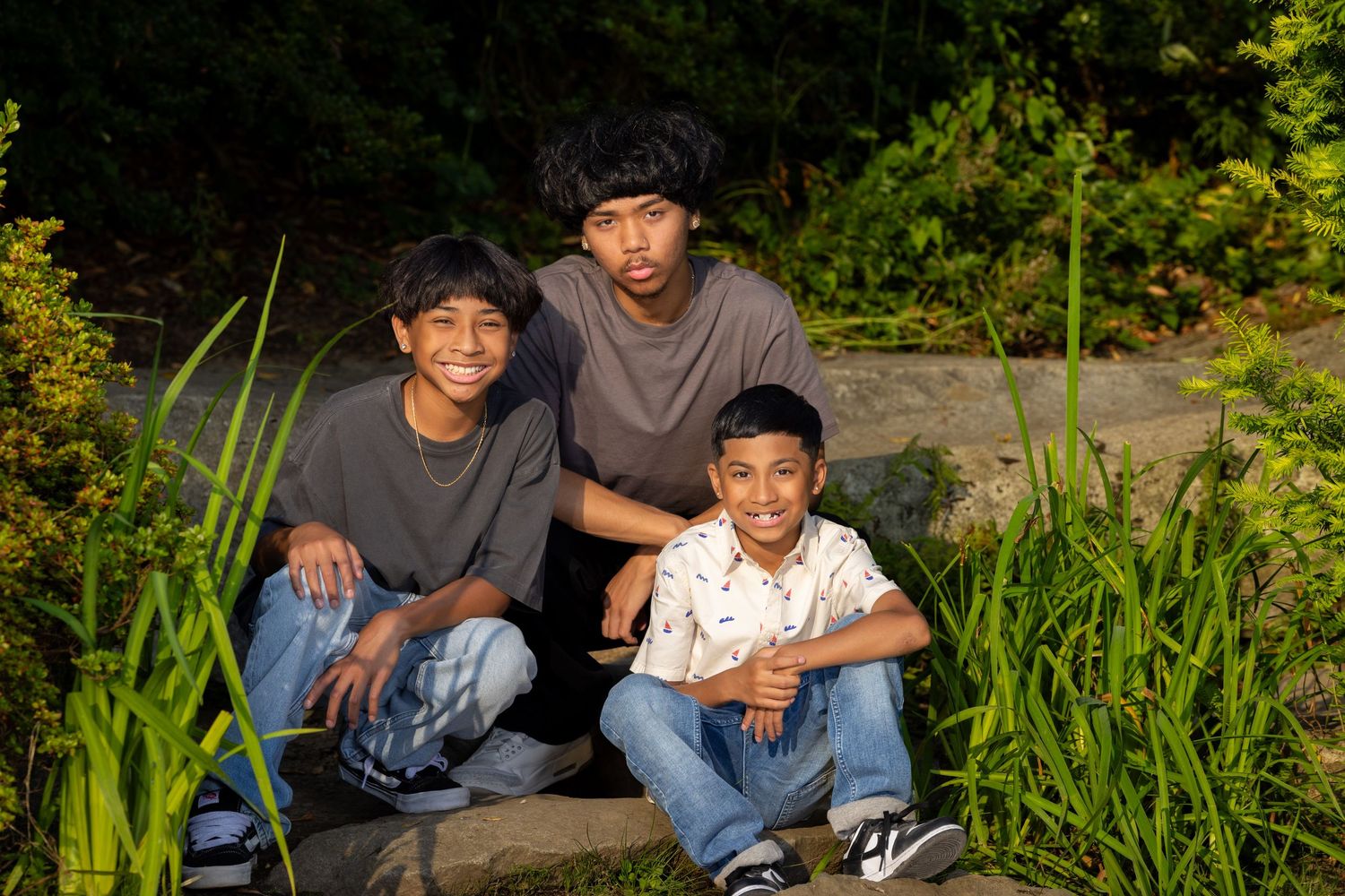 Three people sitting together on stone steps surrounded by tall grass.