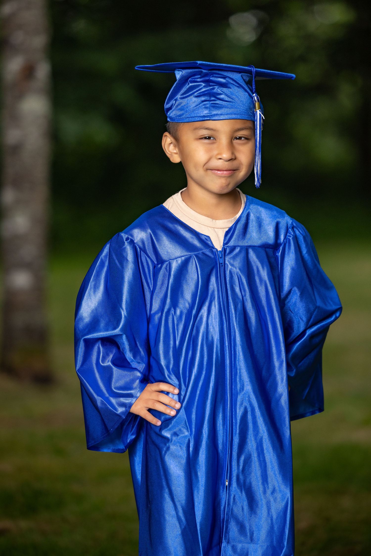 Young graduate wearing bright blue cap and gown poses for photos outdoors.