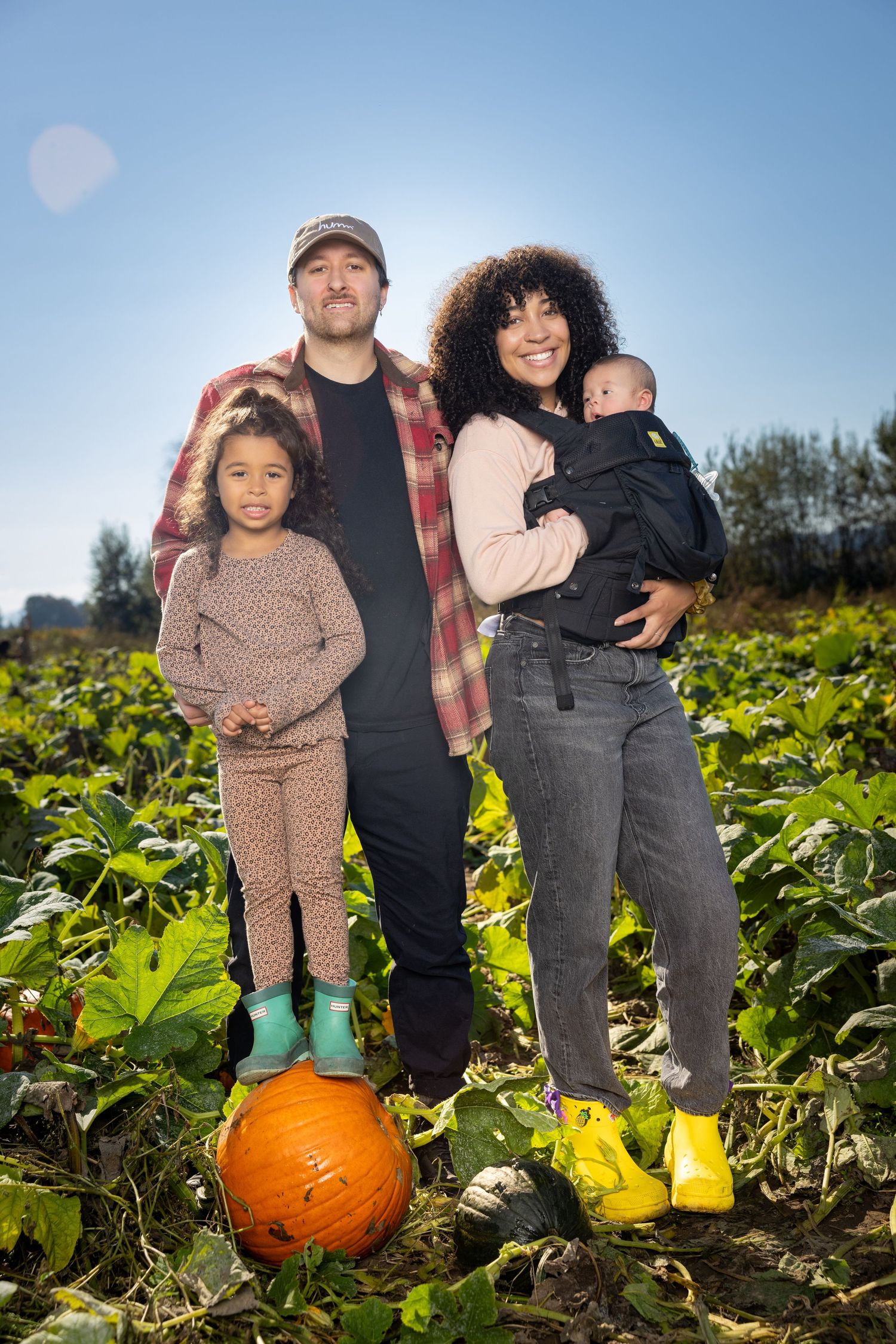 A family poses together in a pumpkin patch on a sunny autumn day.