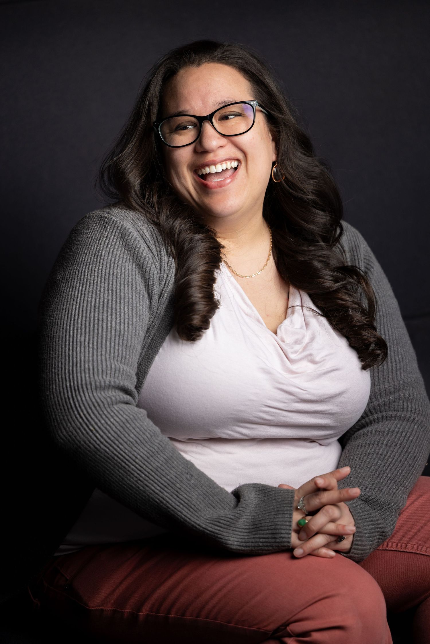 Studio portrait against dark background with grey sweater and white top.