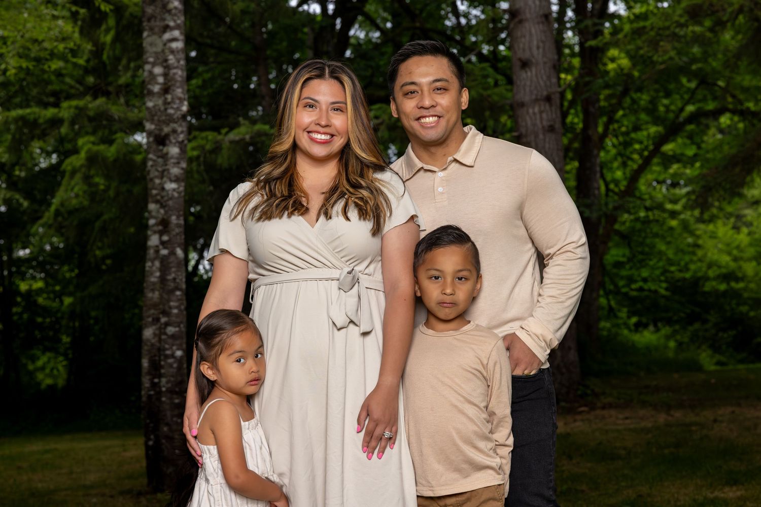 A family poses together in coordinated neutral outfits against a wooded background.