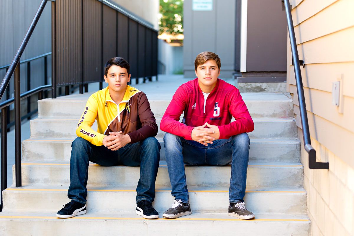 Two teenage boys sitting on outdoor steps, one in yellow jacket and one in red hoodie, posing for a portrait photo.