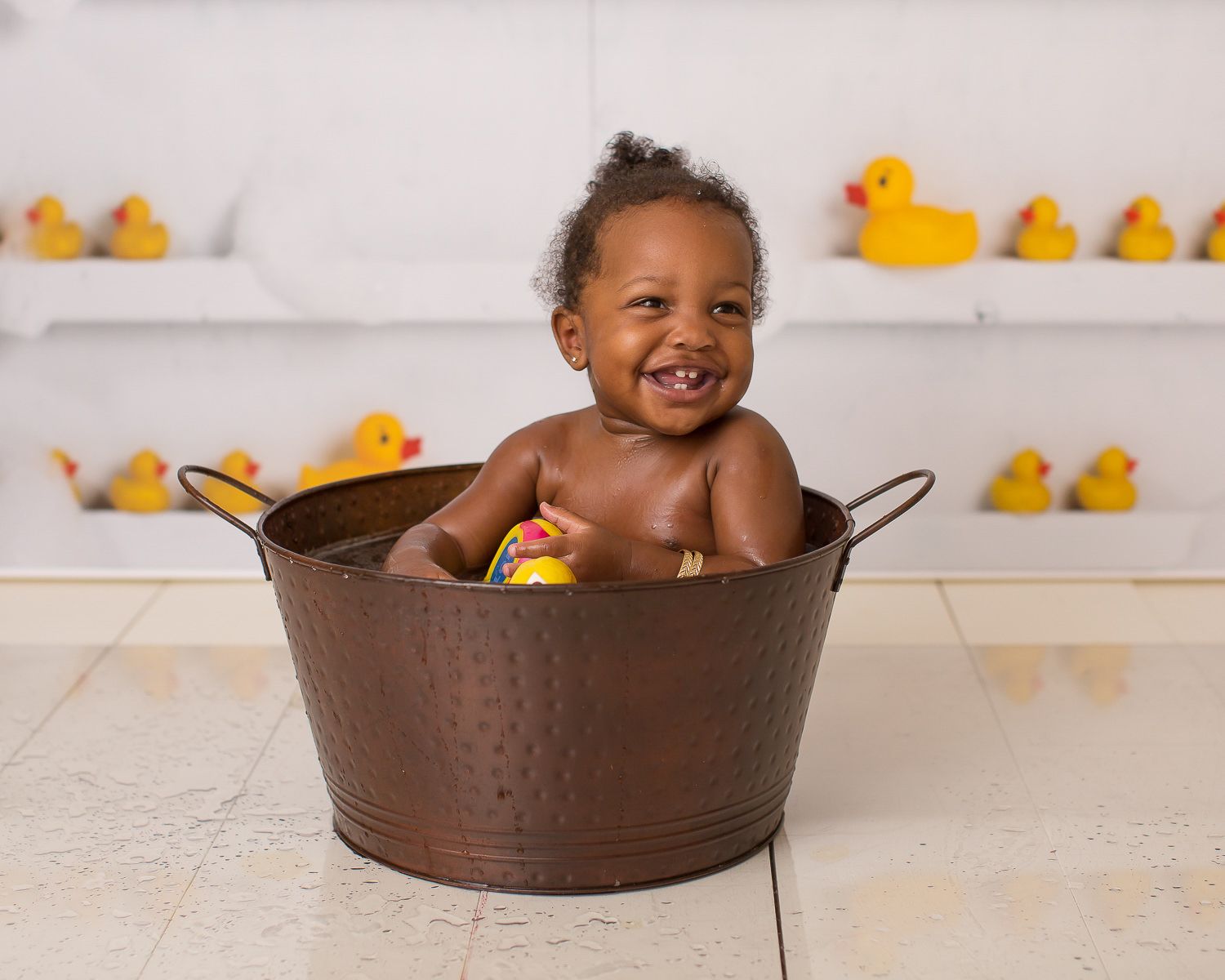 Happy baby boy smiling in a copper tub surrounded by rubber ducks.