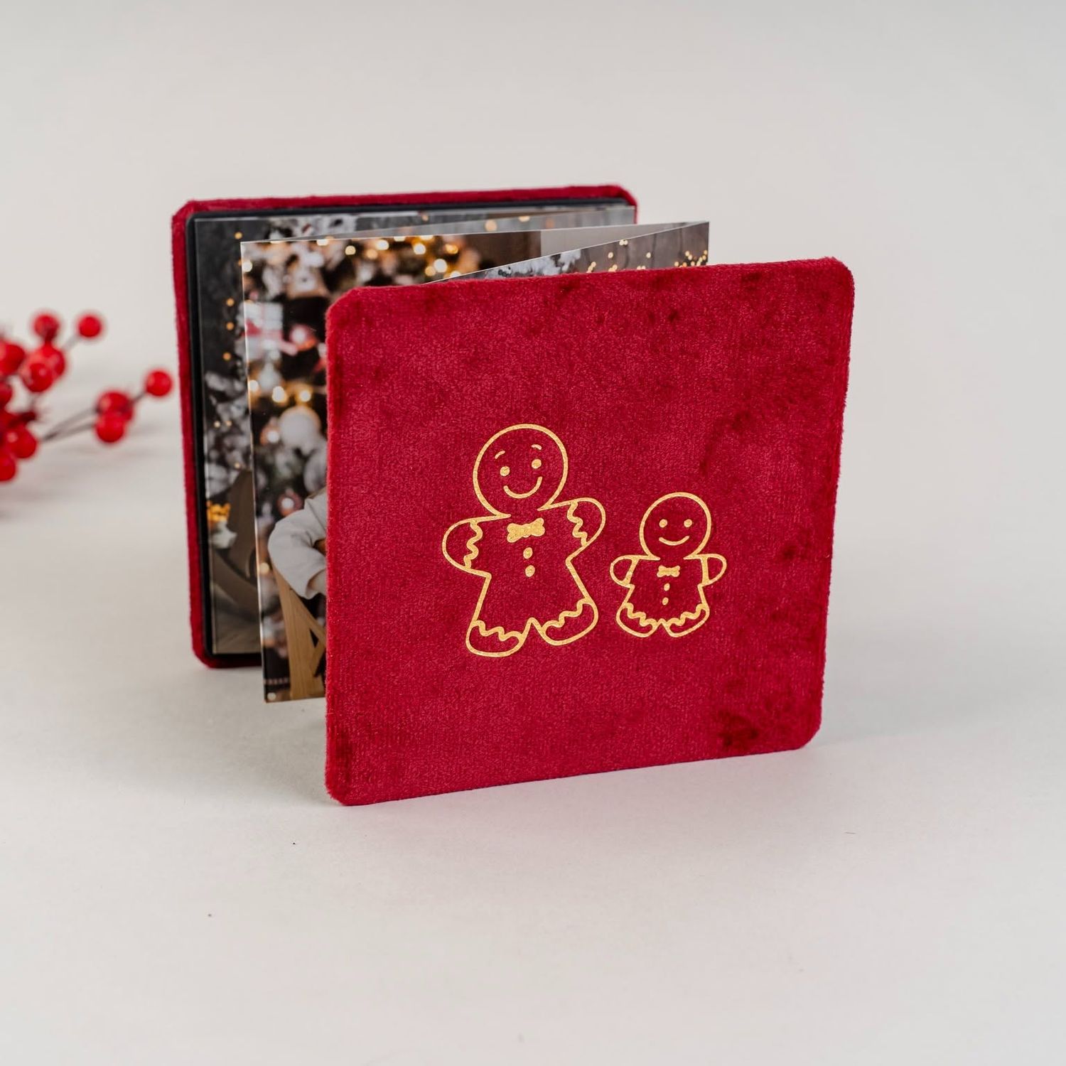 Red velvet mini photo album with gold embroidered gingerbread man and woman design, displayed open with Christmas photos inside.