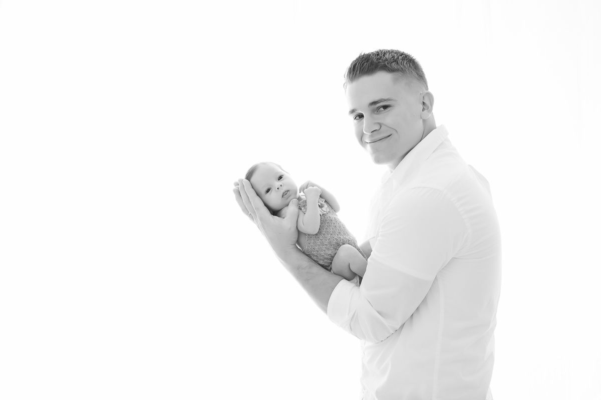 Black and white photo of father in white shirt cradling newborn baby.