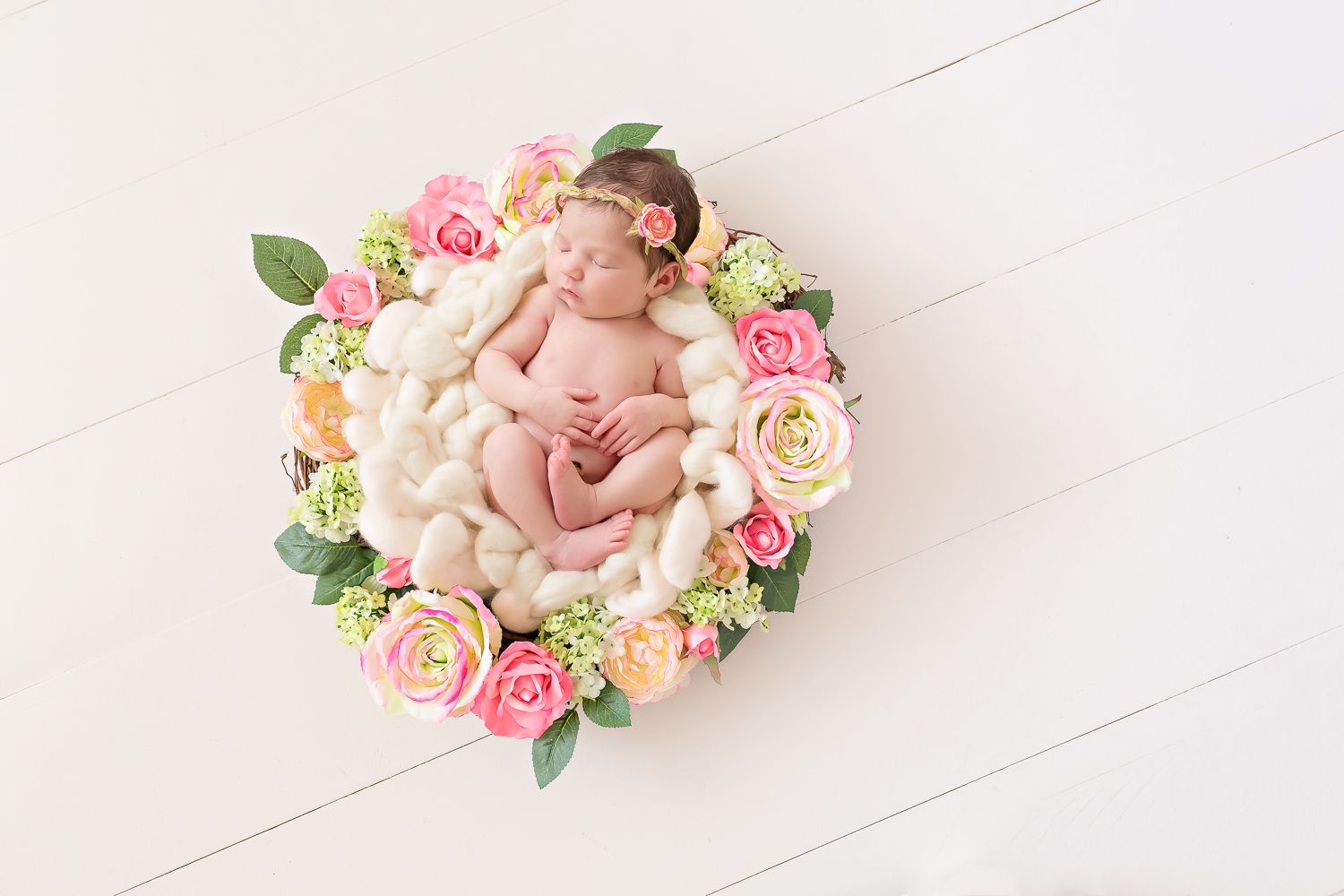 Newborn baby girl sleeping in a round bowl surrounded by colorful pink and orange flowers.