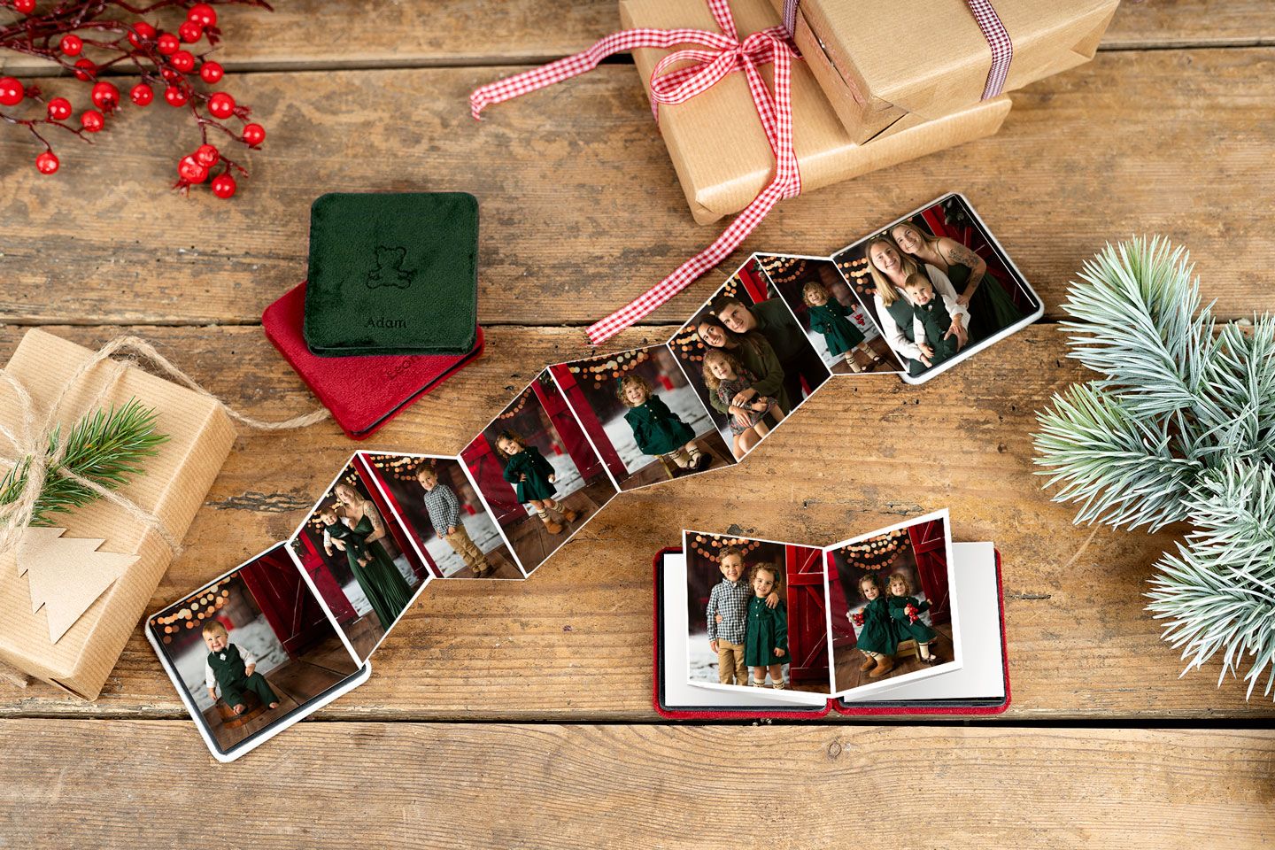Accordion photo book with Christmas family photos displayed open on a rustic wooden table with holiday gifts and greenery.