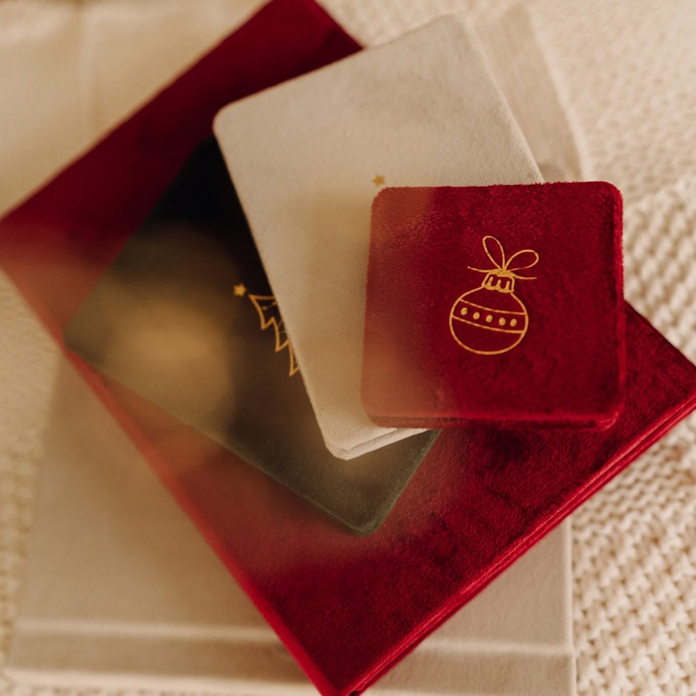 Red velvet gift box with gold Christmas ornament embossed jewelry pouch and frosted card on white surface.