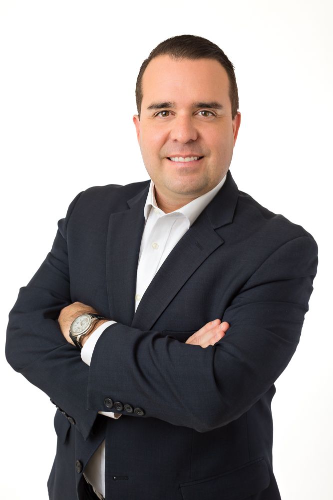 Professional businessman in dark blazer smiling with arms crossed against white background.