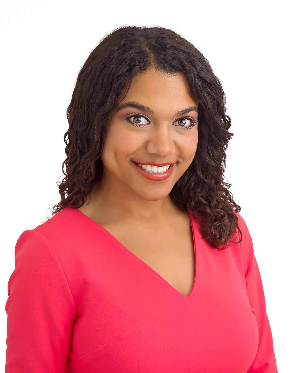 Professional headshot of smiling young woman with curly hair wearing a bright pink blouse.