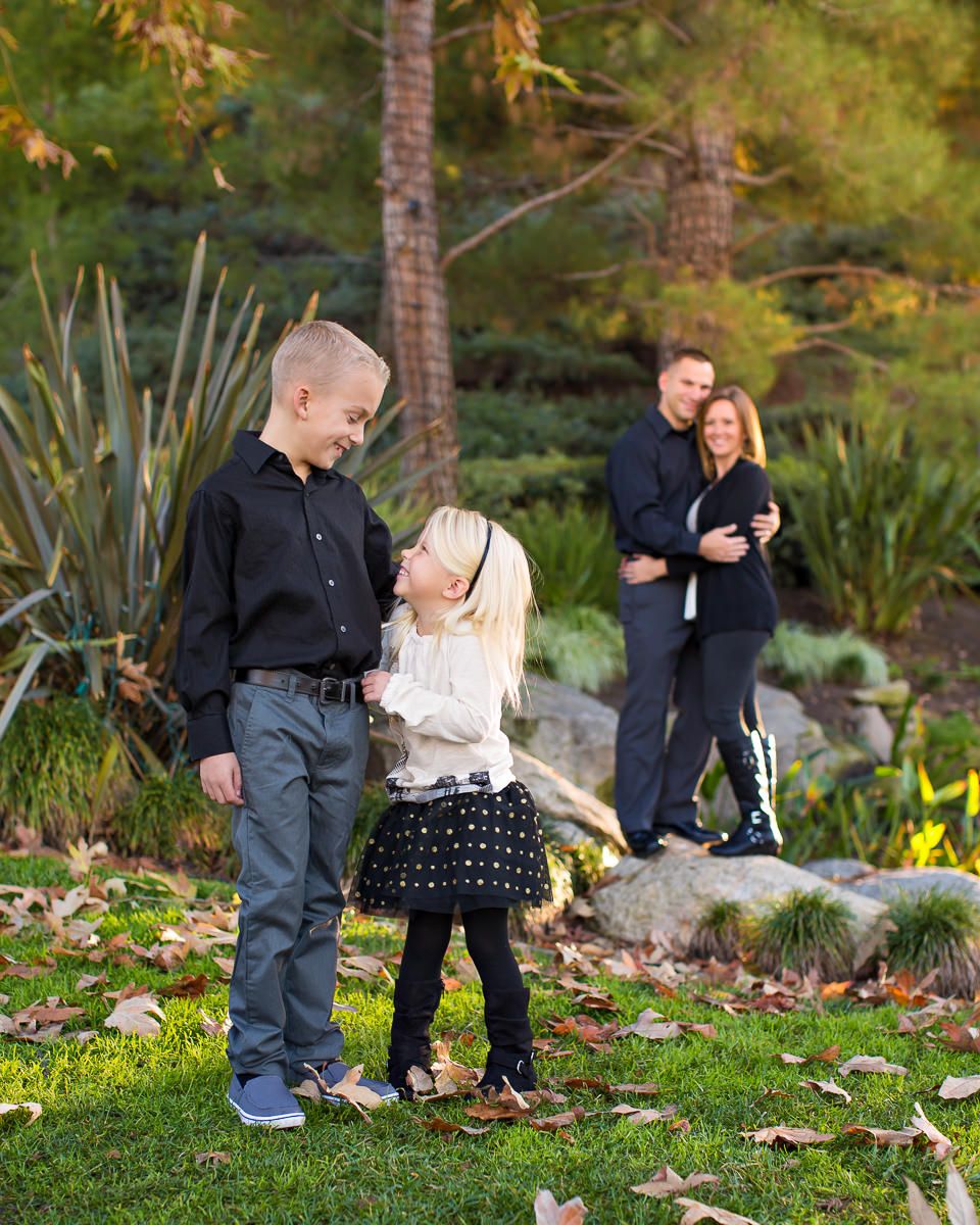 Family portrait with two children playing in a lush green park while parents embrace in the background.