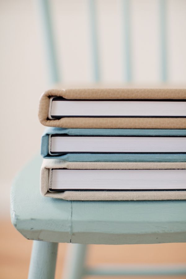 Stack of four elegant linen-covered photo books in neutral tones on a light blue wooden chair.