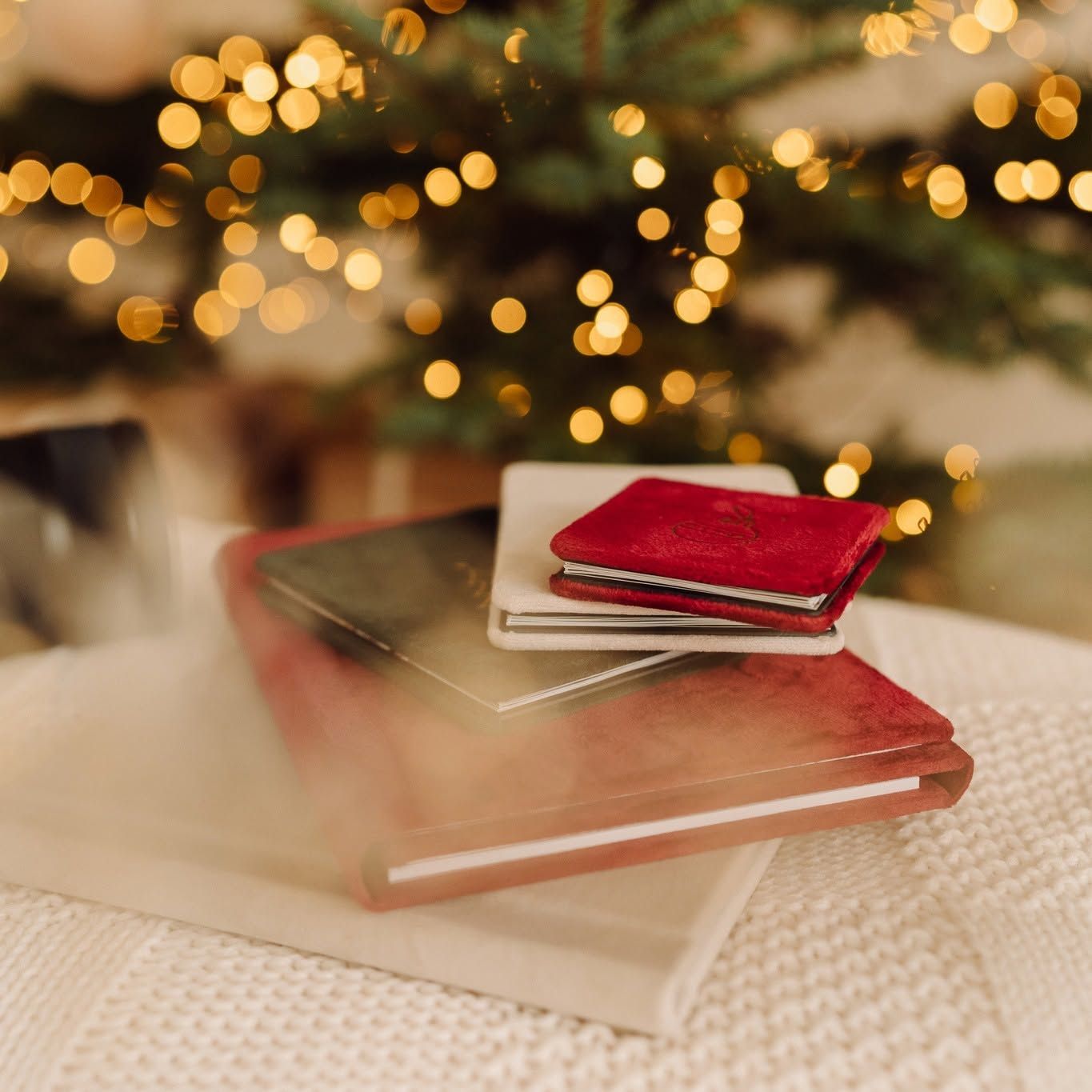 Stack of red and gray notebooks on a knit blanket with bokeh Christmas tree lights in the background.