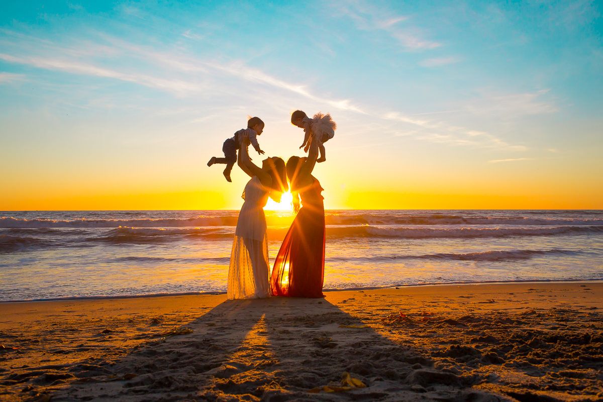 Silhouette of a family with two babies held aloft against a stunning golden beach sunset.