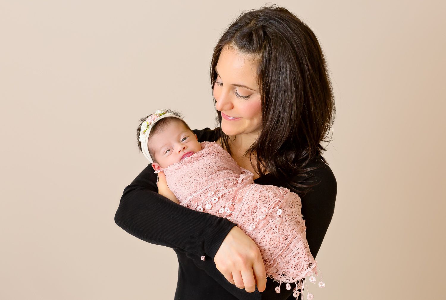 Mother in black top tenderly holding sleeping newborn baby wrapped in pink knit swaddle.