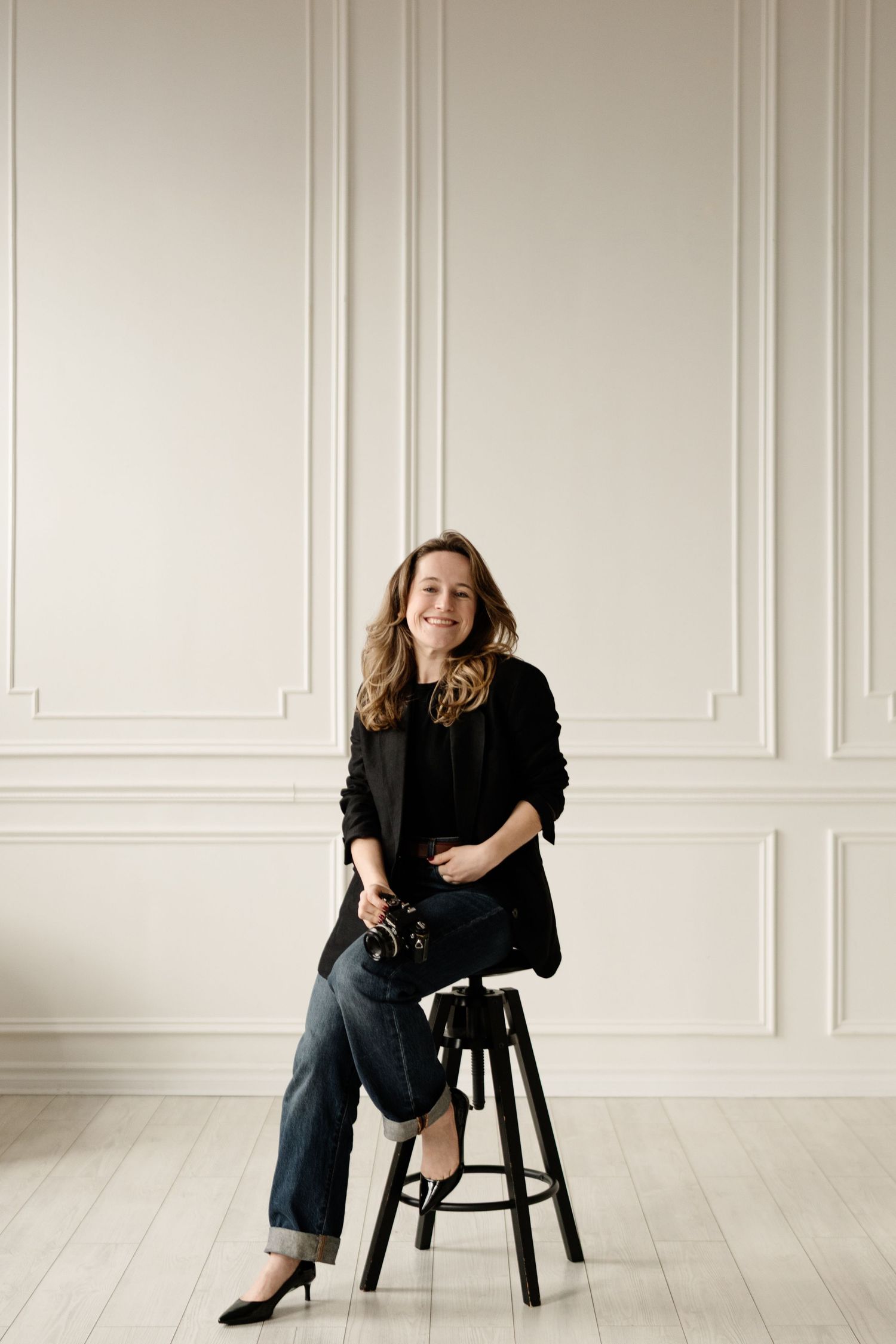 Aliza Dworkind portrait. Montreal films ending photographer sitting on black stool, smiling, holding a film camera.