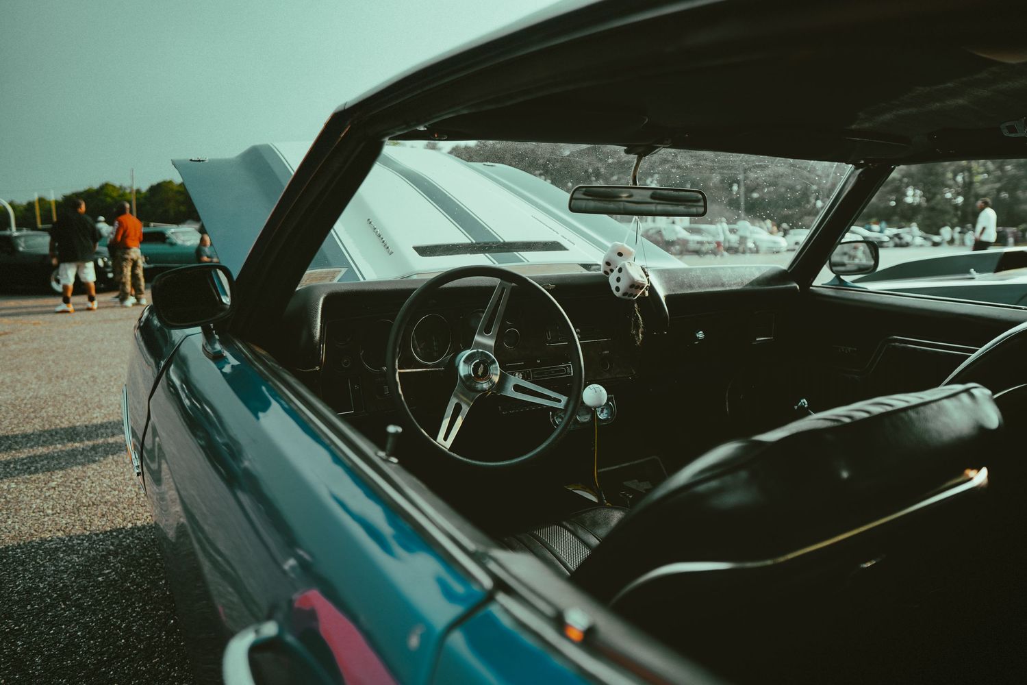 View through open window of vintage convertible car showing black interior and steering wheel against turquoise backdrop.